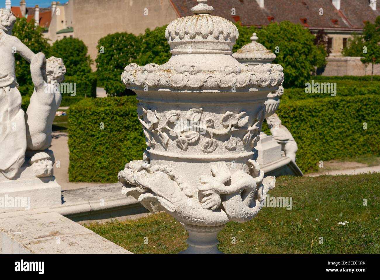 Vista di un vaso da giardino in pietra decorato con intricate incisioni di creature marine e fogliame presso i giardini del Palazzo Belvedere con statue di cherubini e. Foto Stock