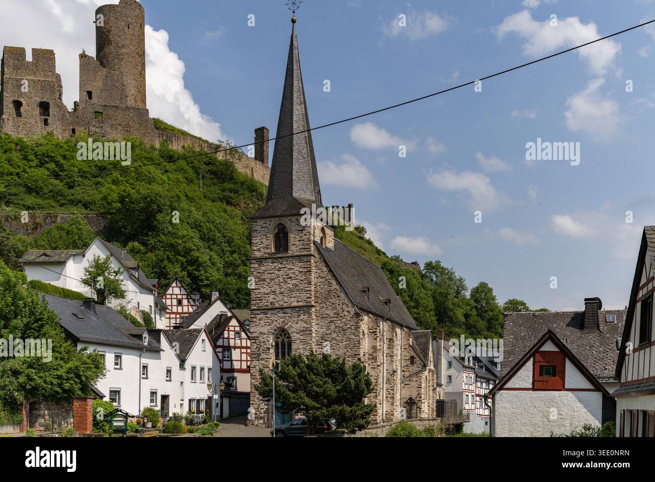 Vista della Dreifaltigkeitskirche e delle case a graticcio con rovine medievali del castello su una lussureggiante collina verde a Monreal, Renania-Palatinato, Germania. Foto Stock