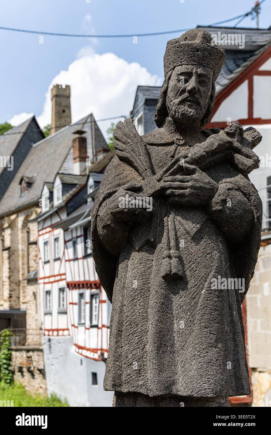 Vista della statua in pietra di San Giovanni Nepomuceno con le tradizionali case in legno e una torre medievale del castello sotto un cielo blu a Monreal, Rhinela Foto Stock