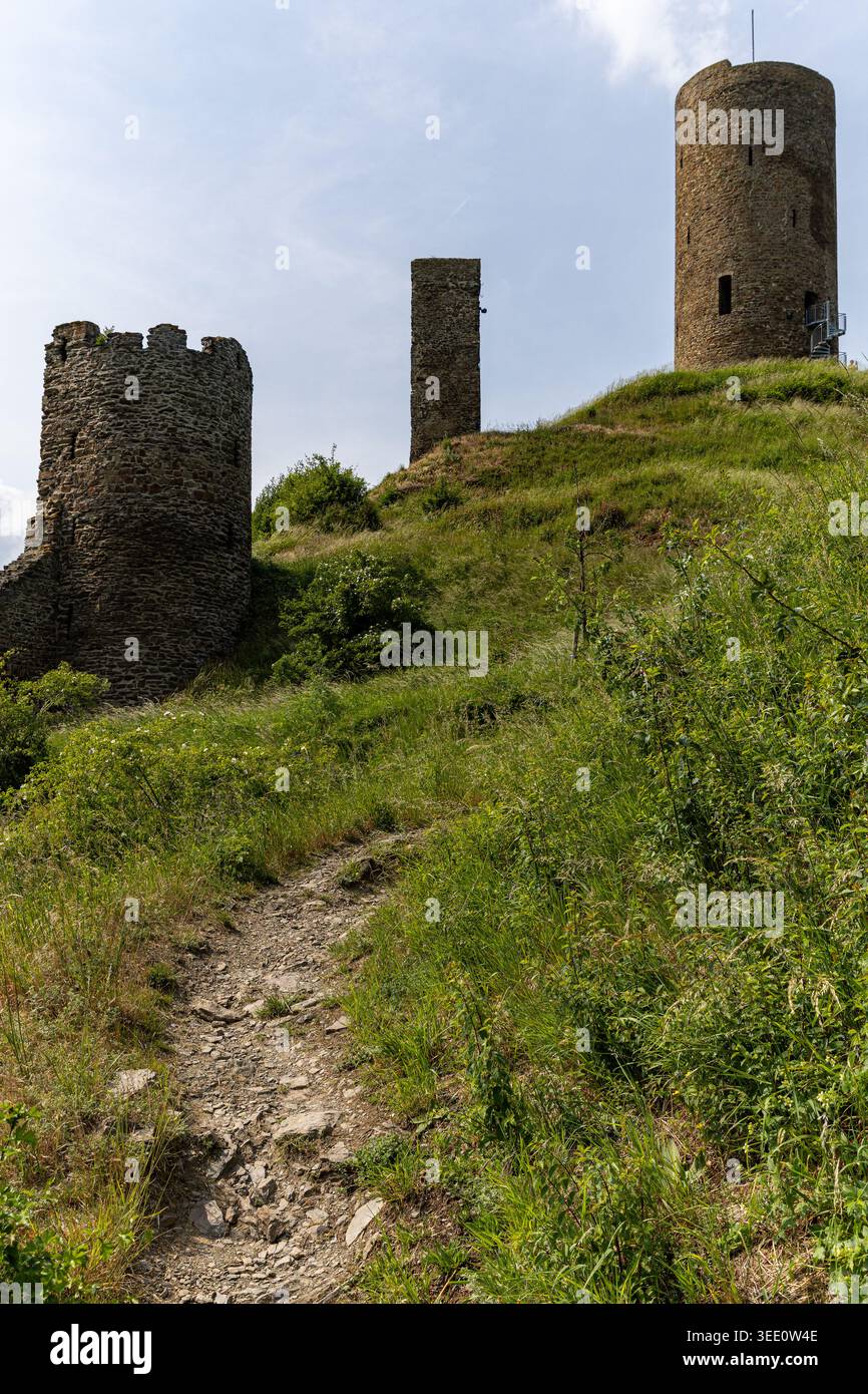 Vista delle rovine del castello di Monreal con antiche torri di pietra su una collina erbosa sotto un cielo luminoso Monreal, Renania-Pfalz, Germania. Foto Stock