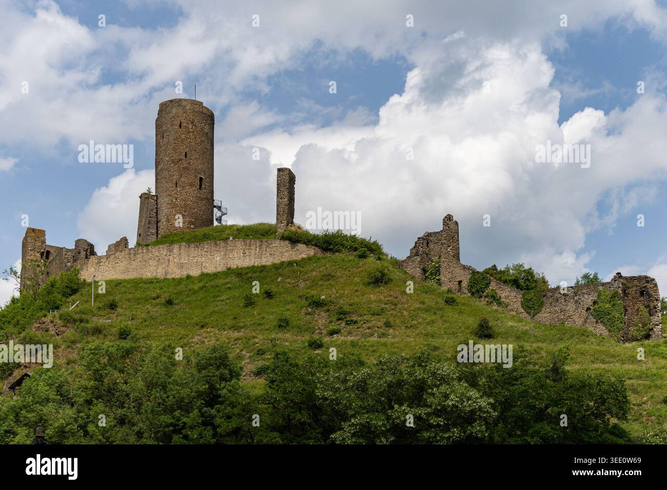 Vista delle storiche rovine del Castello di Monreal con la sua imponente torre in pietra e le pareti sbriciolate su una collina verde sotto un cielo nuvoloso Monreal, Rheinland-PFA Foto Stock
