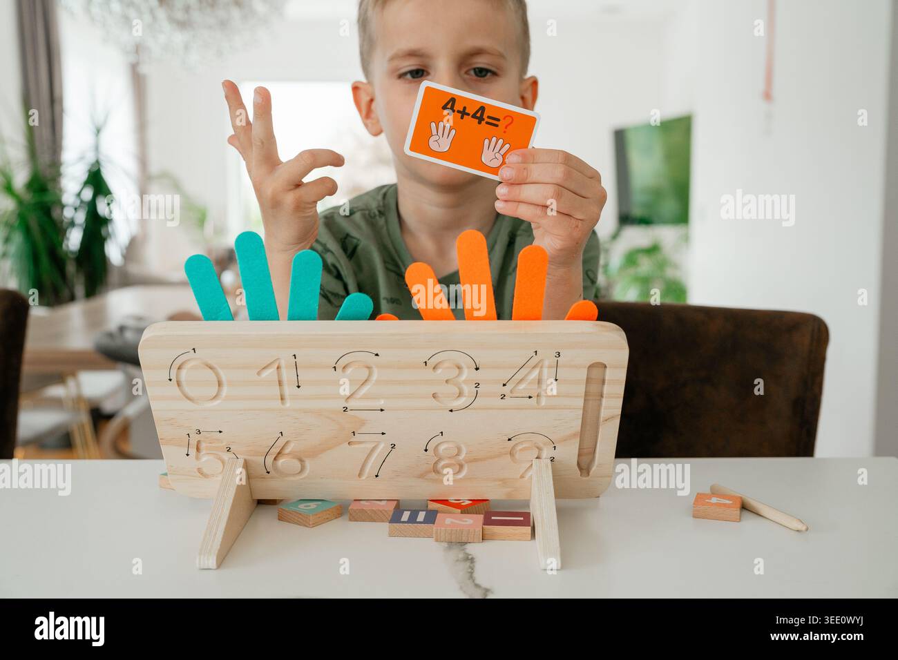 Bambino che tiene in mano una flashcard matematica durante l'aggiunta di apprendimento. Giocattoli didattici e ausili visivi aiutano a migliorare la comprensione dei concetti aritmetici di base. Foto Stock
