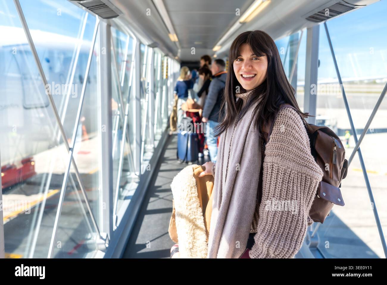 Donna sorridente mentre sali a bordo dell'aereo attraverso il ponte del jet Foto Stock