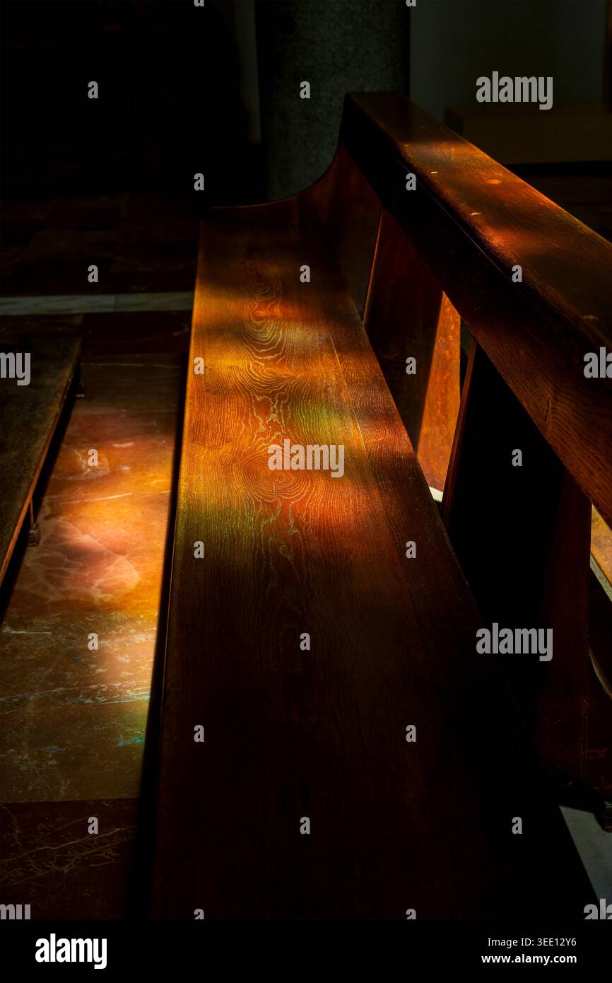 Luce colorata da una finestra di vetro colorato che illumina un pew di legno all'interno di una chiesa. Foto Stock