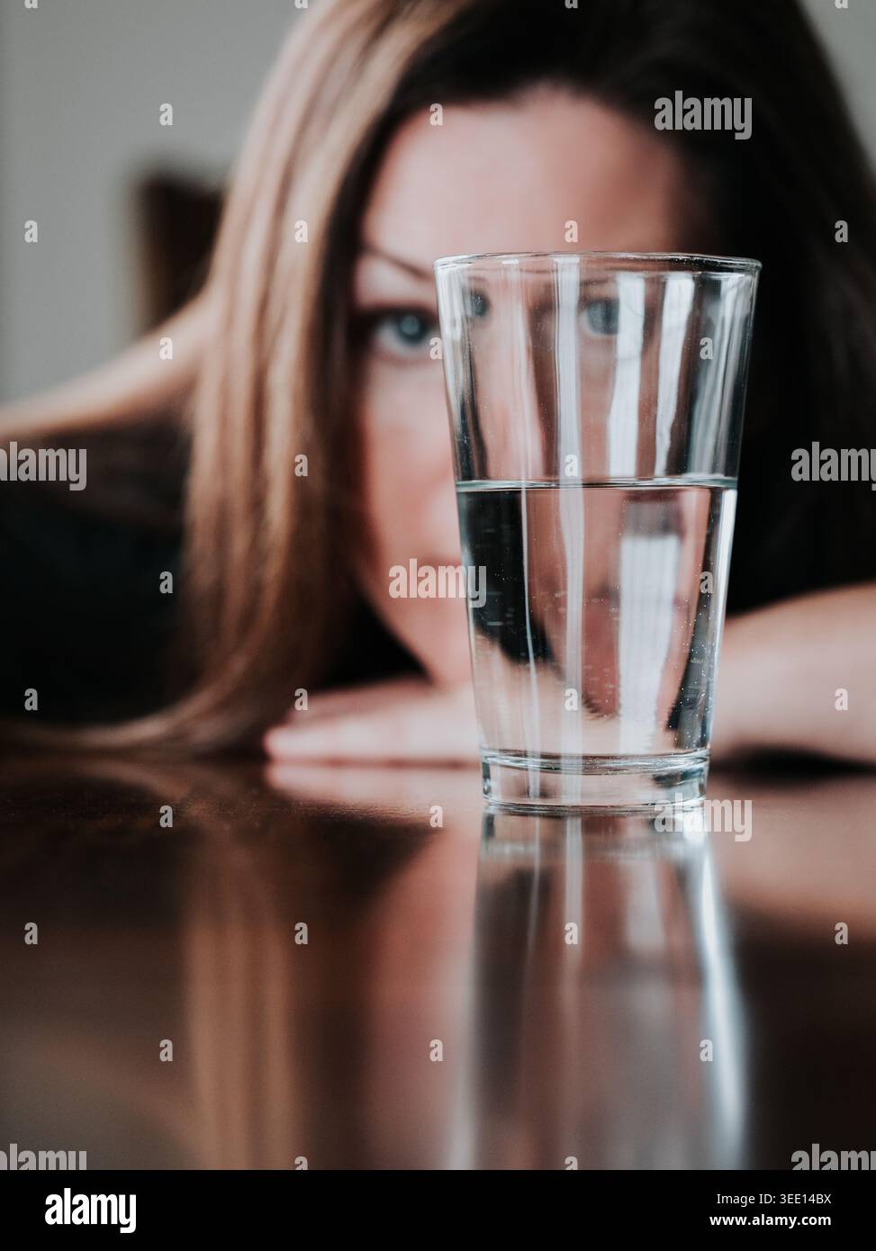 Donna che guarda mezzo bicchiere d'acqua pieno su un tavolo. Foto Stock