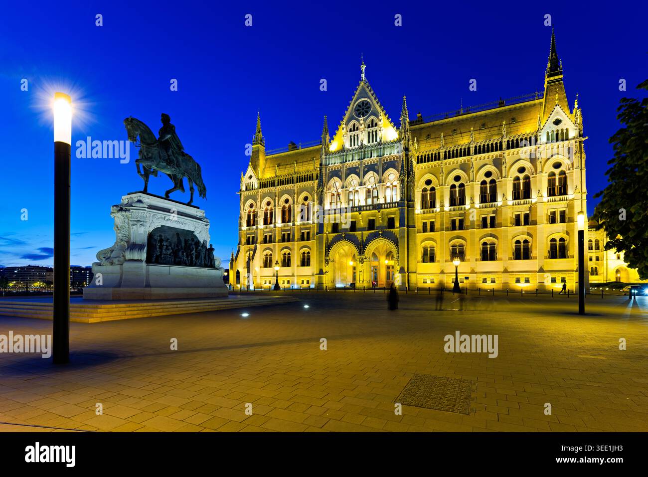 L'edificio del Parlamento di Budapest è illuminato di notte mentre una statua si trova in primo piano. La scena mostra un cielo sereno. Foto Stock
