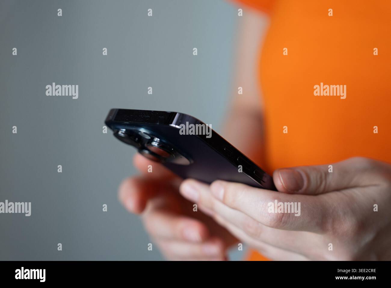 Primo piano di una mano che regge uno smartphone nero su uno sfondo arancione brillante, ideale per progetti di marketing di tecnologia, comunicazione e stile di vita digitale. Foto Stock