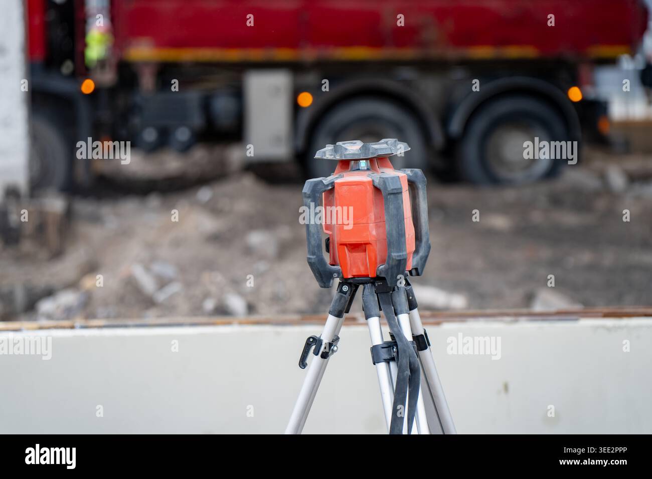 Misurazione della livella laser in piedi su un treppiede in cantiere con carrello in background, utile per la disposizione degli edifici e il flusso di lavoro di misurazione Foto Stock