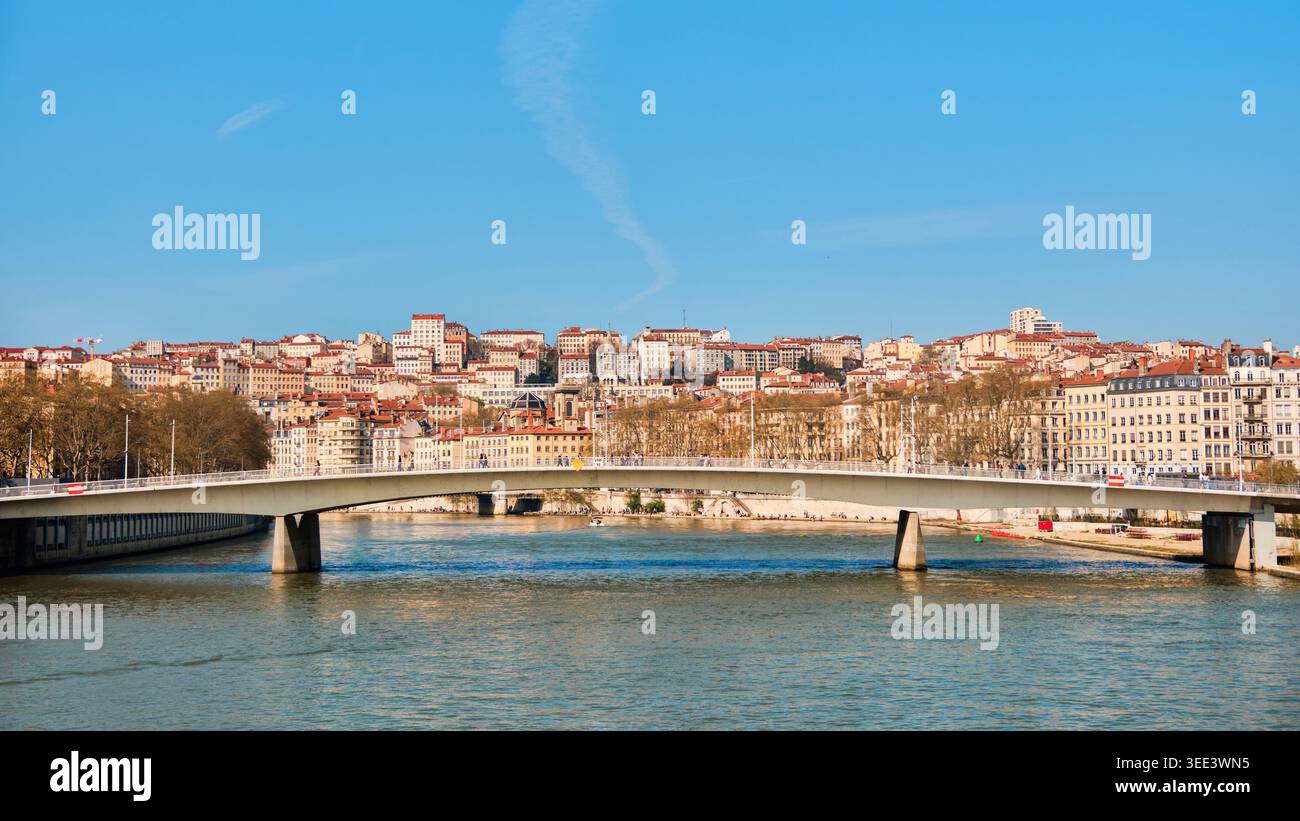 Lione, Francia - 19 marzo 2026: Moderno ponte pedonale che attraversa il fiume Saone con vista sugli storici edifici collinari sotto un cielo azzurro Foto Stock