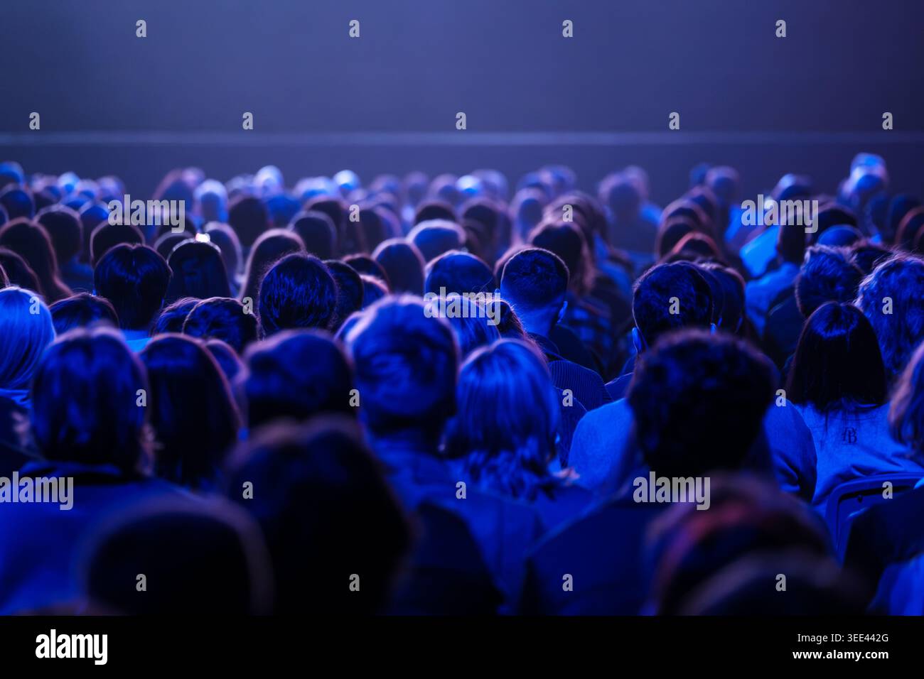 Il grande pubblico seduto è immerso nell'illuminazione blu del palcoscenico, incentrato su spettacoli dal vivo, esperienze condivise e anticipazione collettiva. Foto Stock