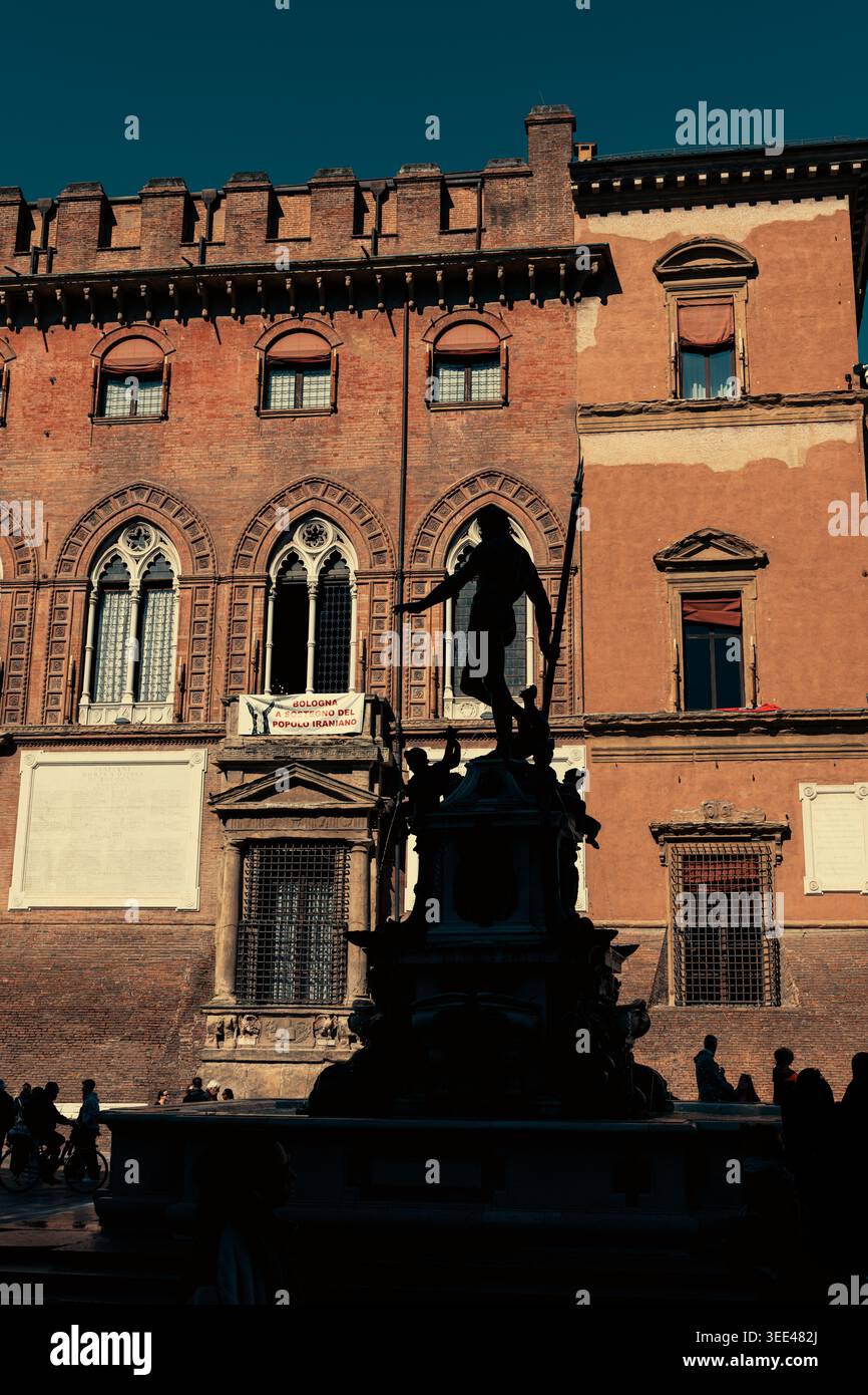 Spettacolare silhouette della Fontana di Nettuno contro una facciata medievale in mattoni in Piazza maggiore, Bologna. La luce solare ad angolo basso cas Foto Stock