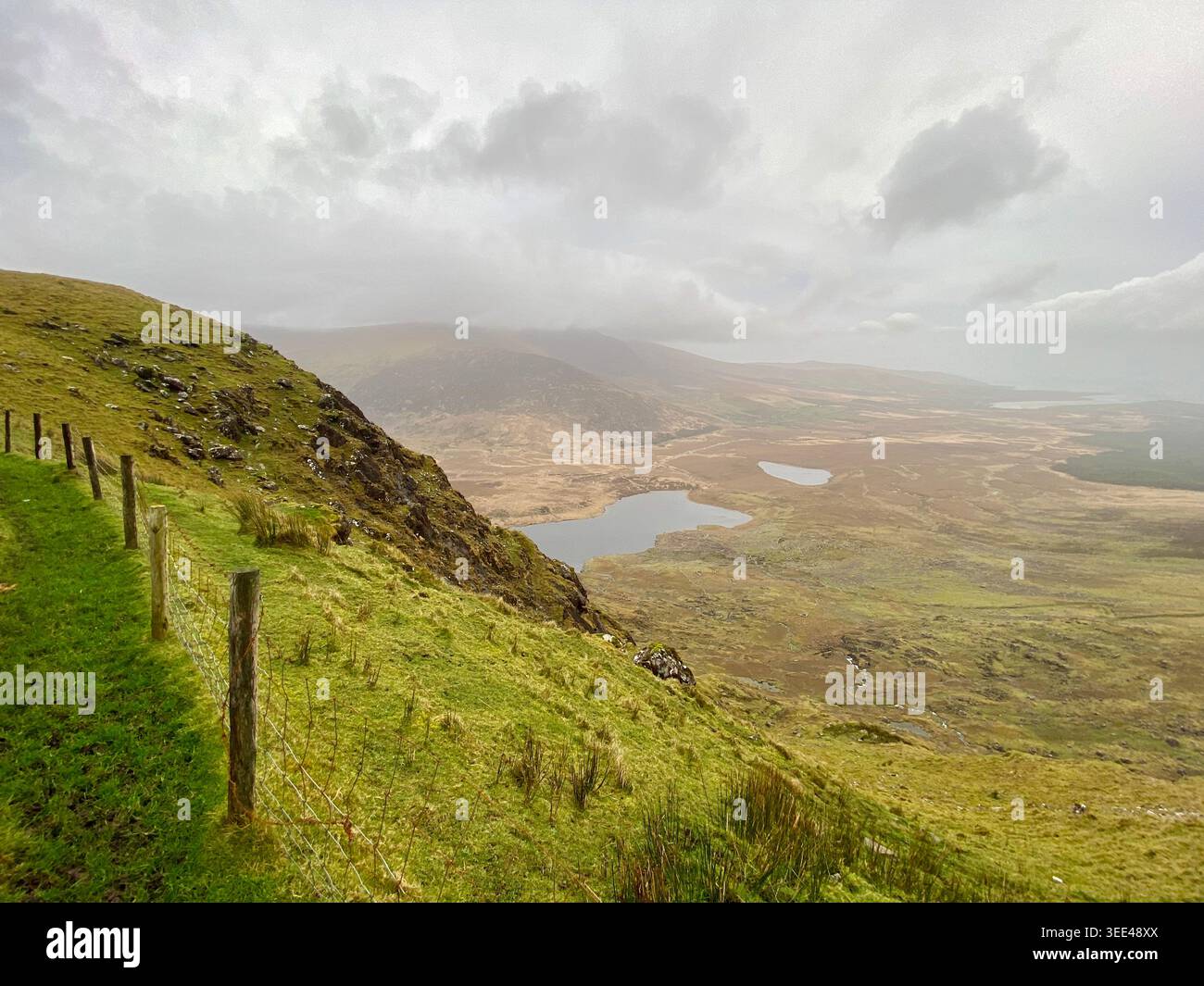 Vista panoramica a nord dal Conor Pass sui laghi glaciali e sulla valle bogland, sulla collina verde con recinzione a filo metallico, sulla penisola di Dingle, Kerry, Irlanda Foto Stock