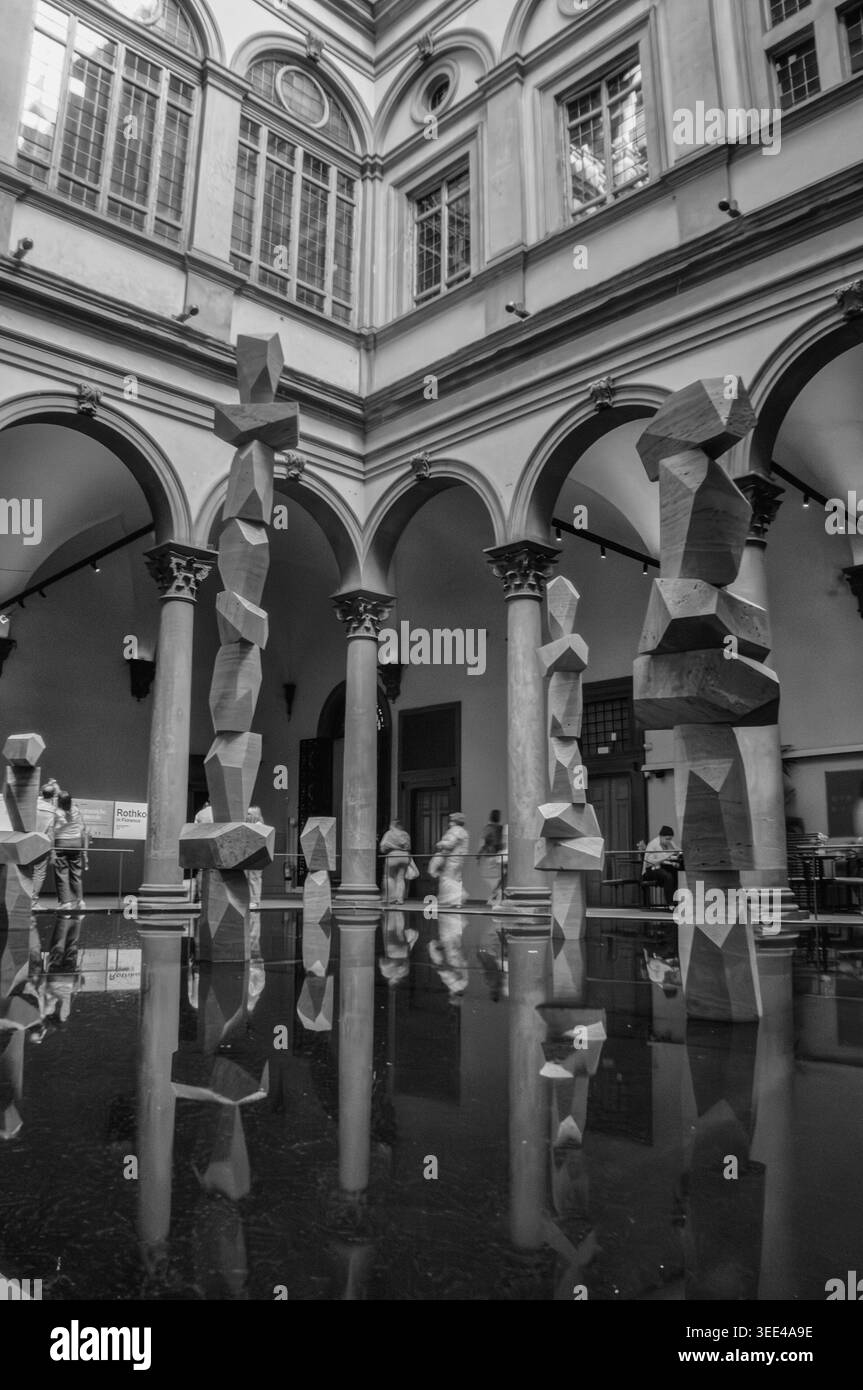 La fotografia in bianco e nero cattura moderne sculture geometriche alte in un'installazione d'acqua riflettente all'interno di un classico cortile italiano. Foto Stock