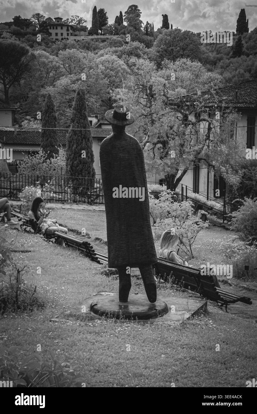 Una foto in bianco e nero cattura una scultura di una figura in un cappello e un lungo cappotto, visto da dietro, posizionato in un parco di Firenze, Italia. La scultura Foto Stock