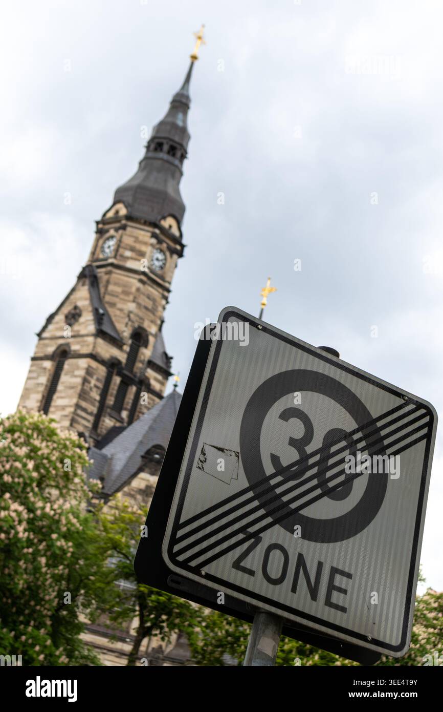 Primo piano di un cartello stradale di 30 km/h alla fine della zona di velocità in primo piano con una guglia sfocata della chiesa storica in pietra sotto un cielo nuvoloso Foto Stock