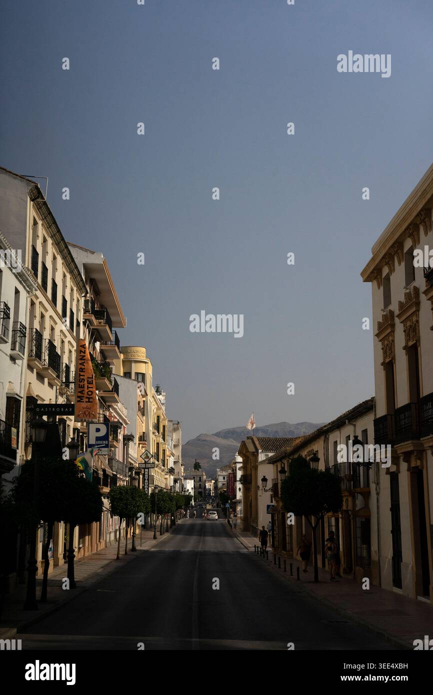 Strada vuota illuminata dal sole nella città andalusa con edifici bianchi e montagne lontane sotto il cielo blu. Foto Stock