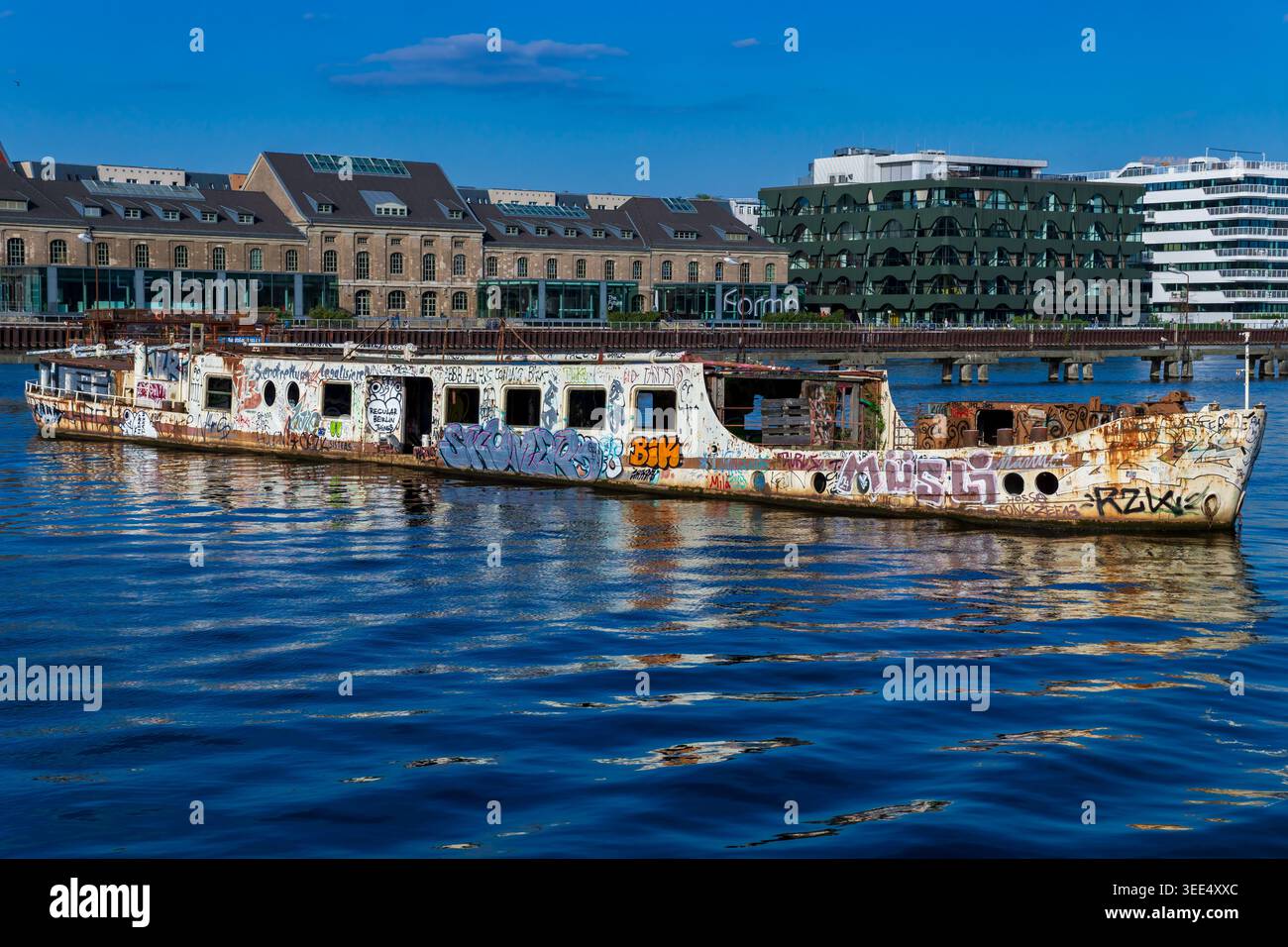 L'ex nave MS Dr. Ingrid Wengler ha ricoperto di graffiti sul fiume Sprea a Berlino, in Germania, con moderni edifici Mediaspree sullo sfondo. Foto Stock