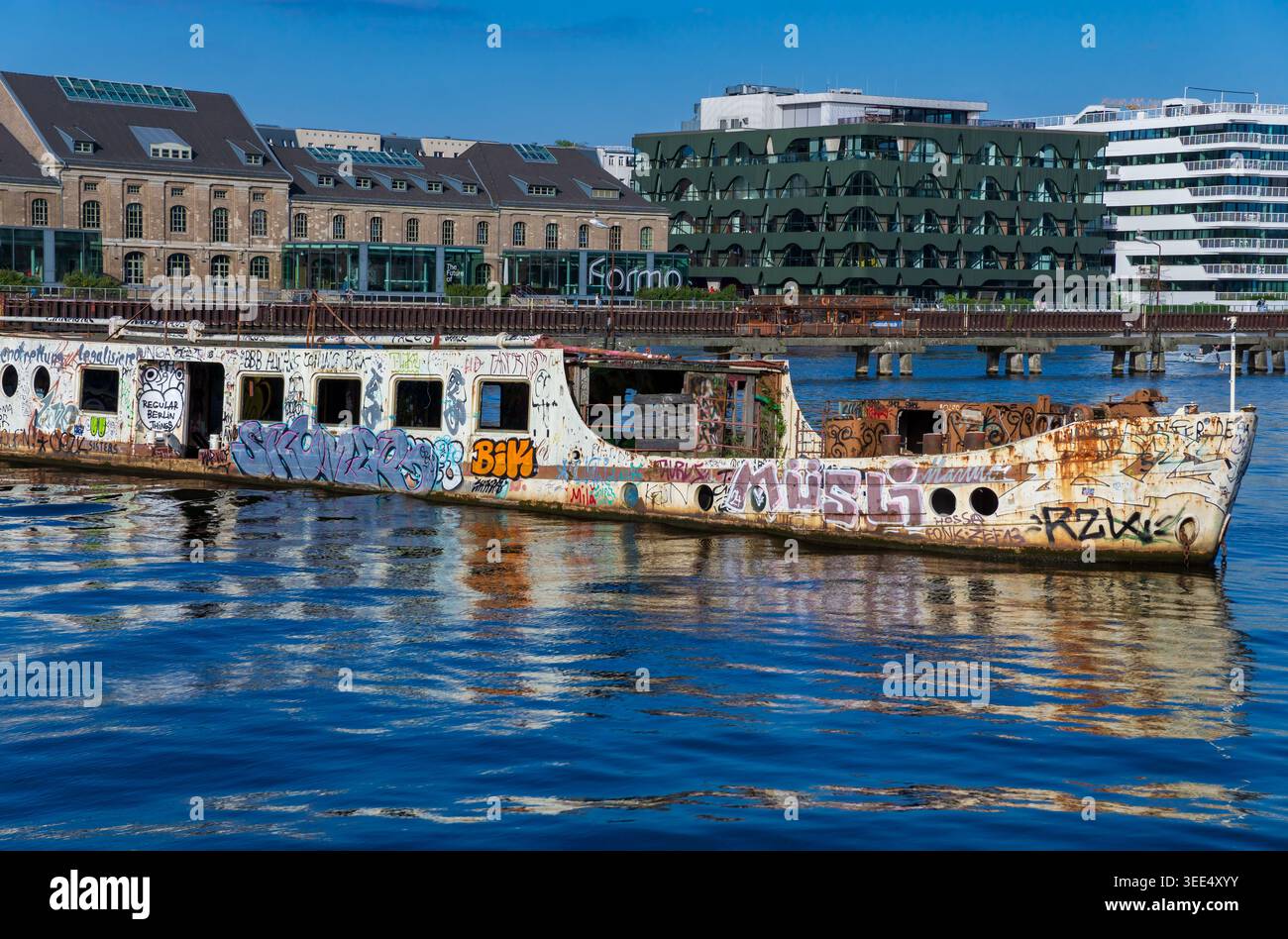 L'ex nave MS Dr. Ingrid Wengler ha ricoperto di graffiti sul fiume Sprea a Berlino, in Germania, con moderni edifici Mediaspree sullo sfondo. Foto Stock