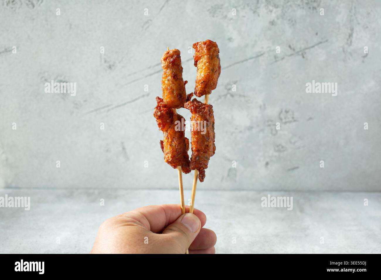 Vista di una mano che tiene degli spiedini di torta di pesce. Foto Stock