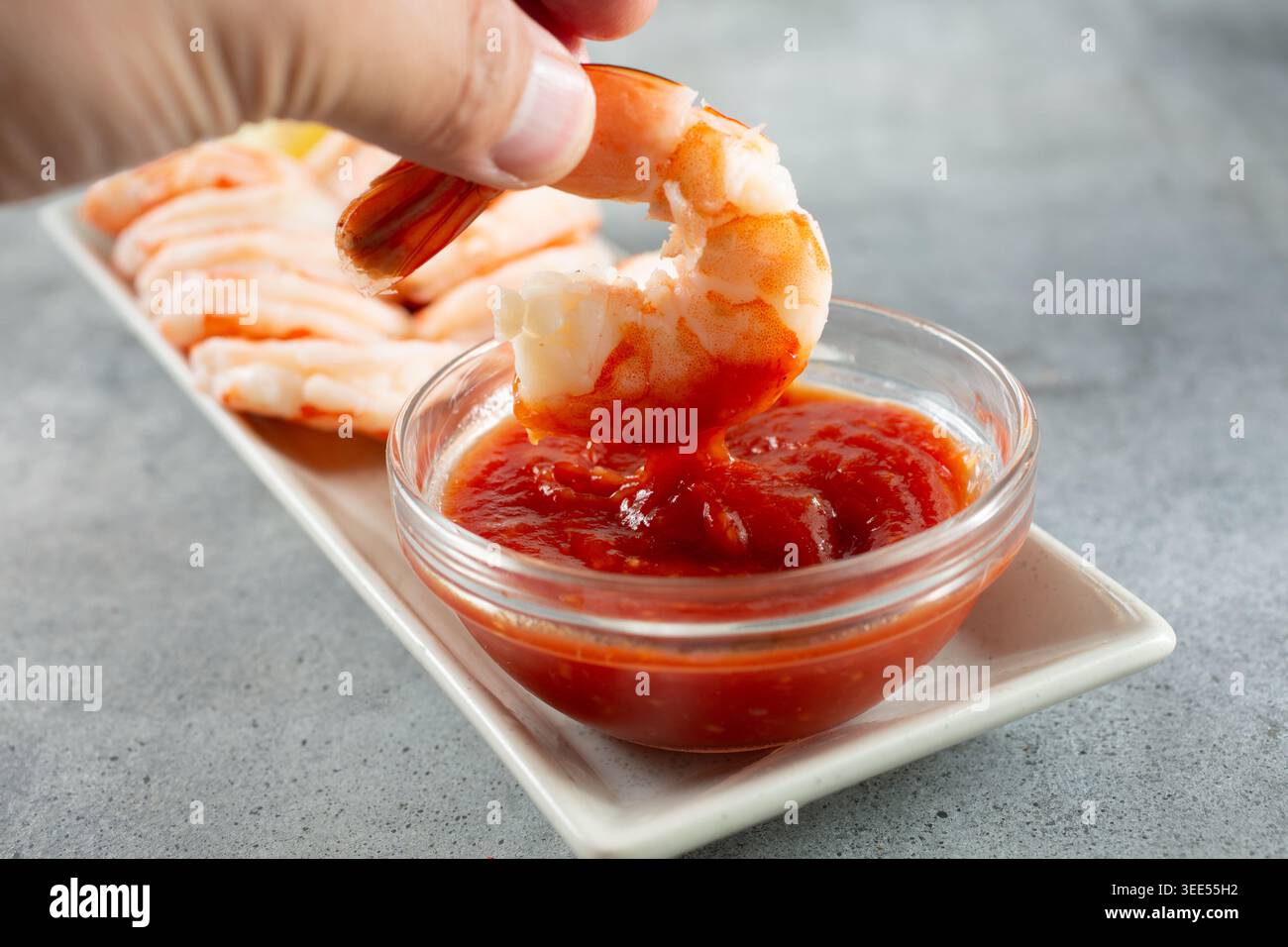 Vista ravvicinata di una mano che immerge un gambero in salsa cocktail. Foto Stock