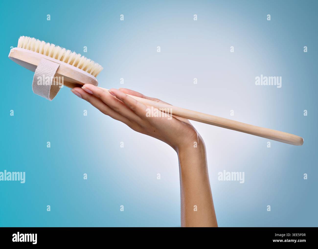 Studio, igiene e mano con spazzola per il corpo, benessere o scrubber con setole naturali per esfoliazione. Sfondo blu, spazio e persona con eco Foto Stock