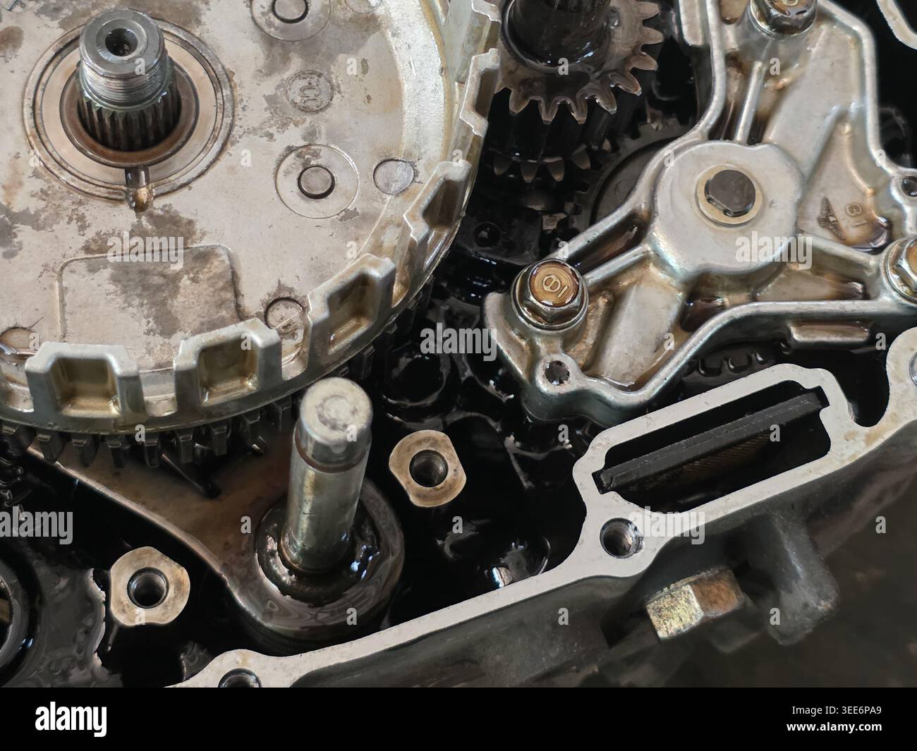 Vista ravvicinata che mostra i complessi meccanismi degli ingranaggi del motore e i macchinari in metallo in attesa di riparazione all'interno dell'officina automobilistica del settore, rivelando il motore interno Foto Stock