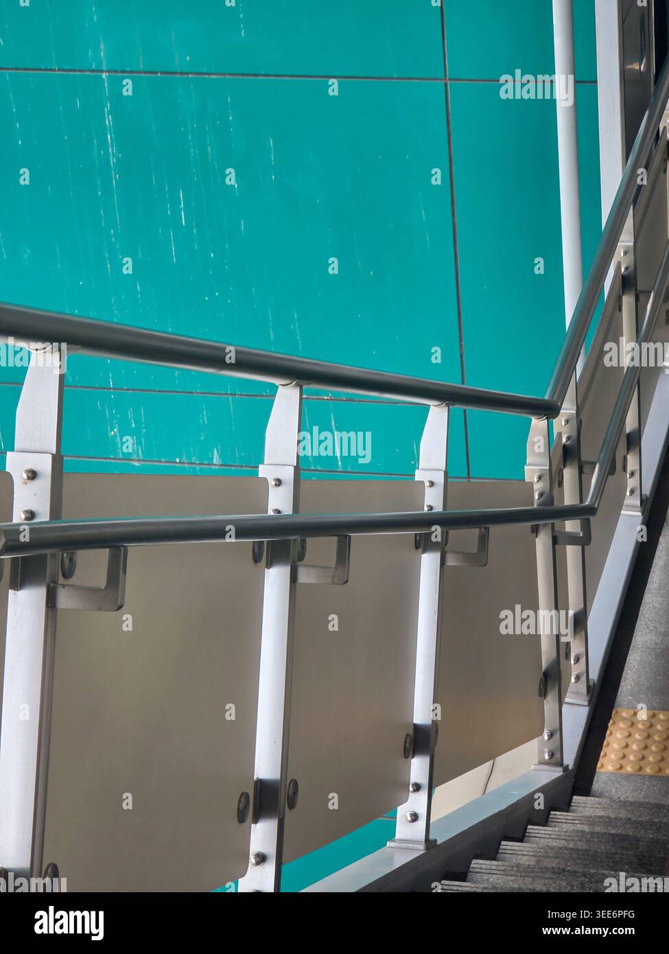 Moderna scala in metallo con corrimano di sicurezza e pannello in vetro che mostra un luminoso sfondo architettonico color verde acqua che trasmette una sensazione di semplicità urbana strutturata Foto Stock