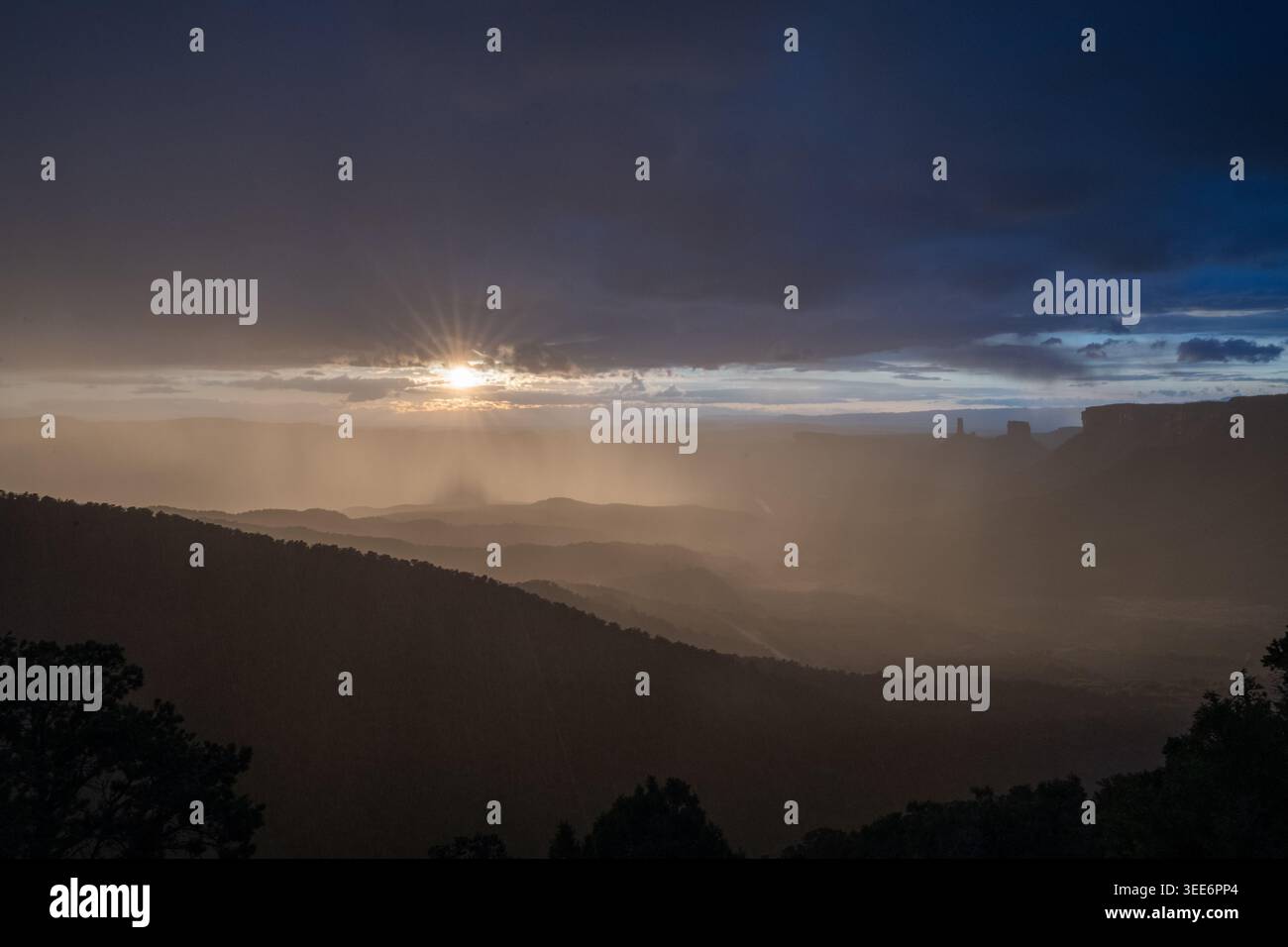 Vista di un'esplosione di sole che si infrangono attraverso nuvole di tempesta scure su una valle desertica con colline sagomate a Moab, Utah, Stati Uniti. Foto Stock