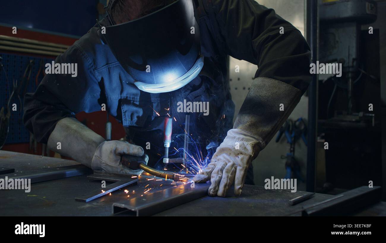Saldatore esperto con esperienza nella fabbricazione di metalli, che utilizza tecniche di saldatura MIG per creare scintille e modellare i componenti metallici. Foto Stock
