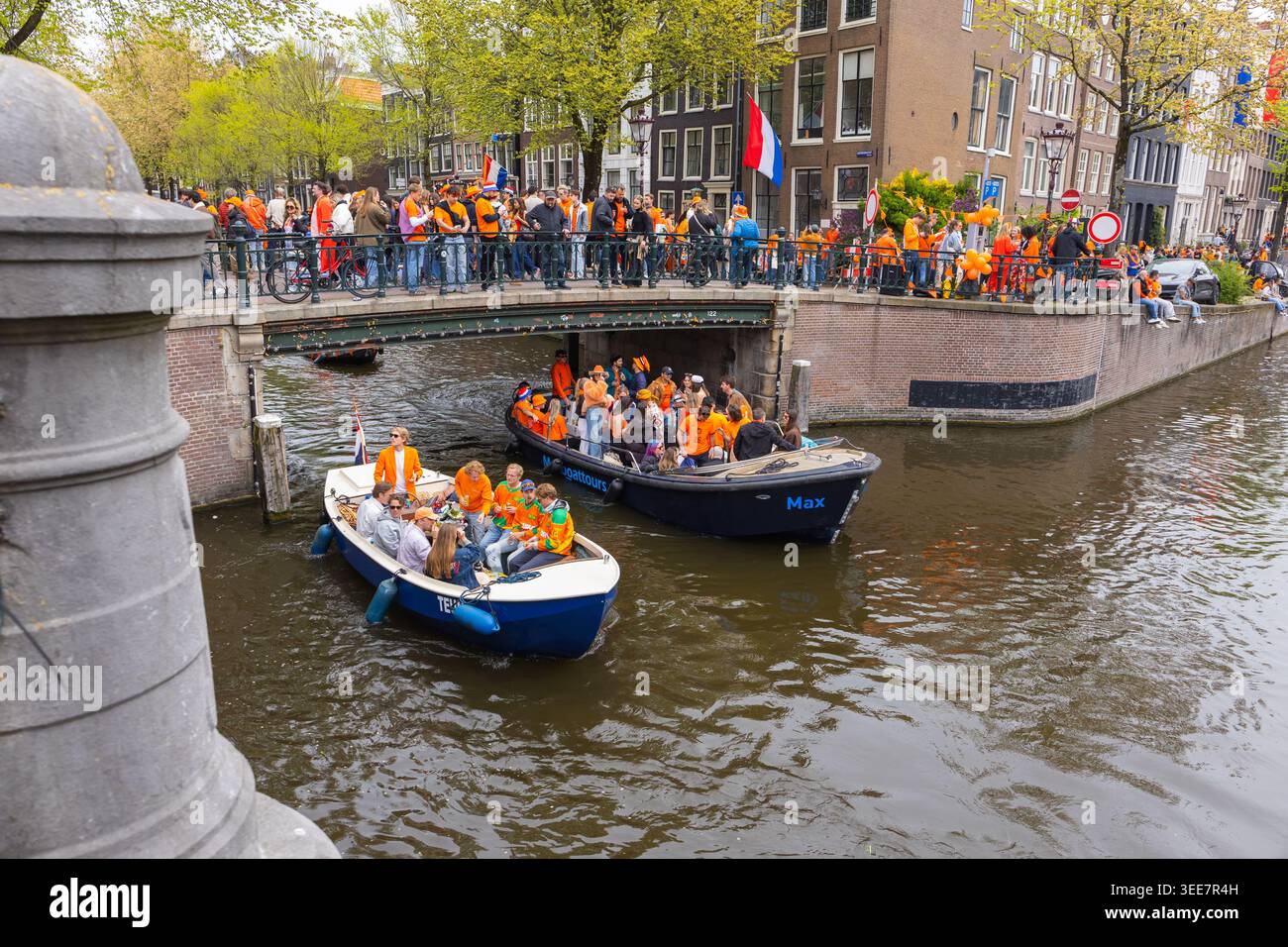 Amsterdam, Paesi Bassi - 27 aprile 2026: La folla è sulla linea dei canali di Amsterdam, mentre le barche piene di festeggiamenti in arancione celebrano il Kings Day. Foto Stock