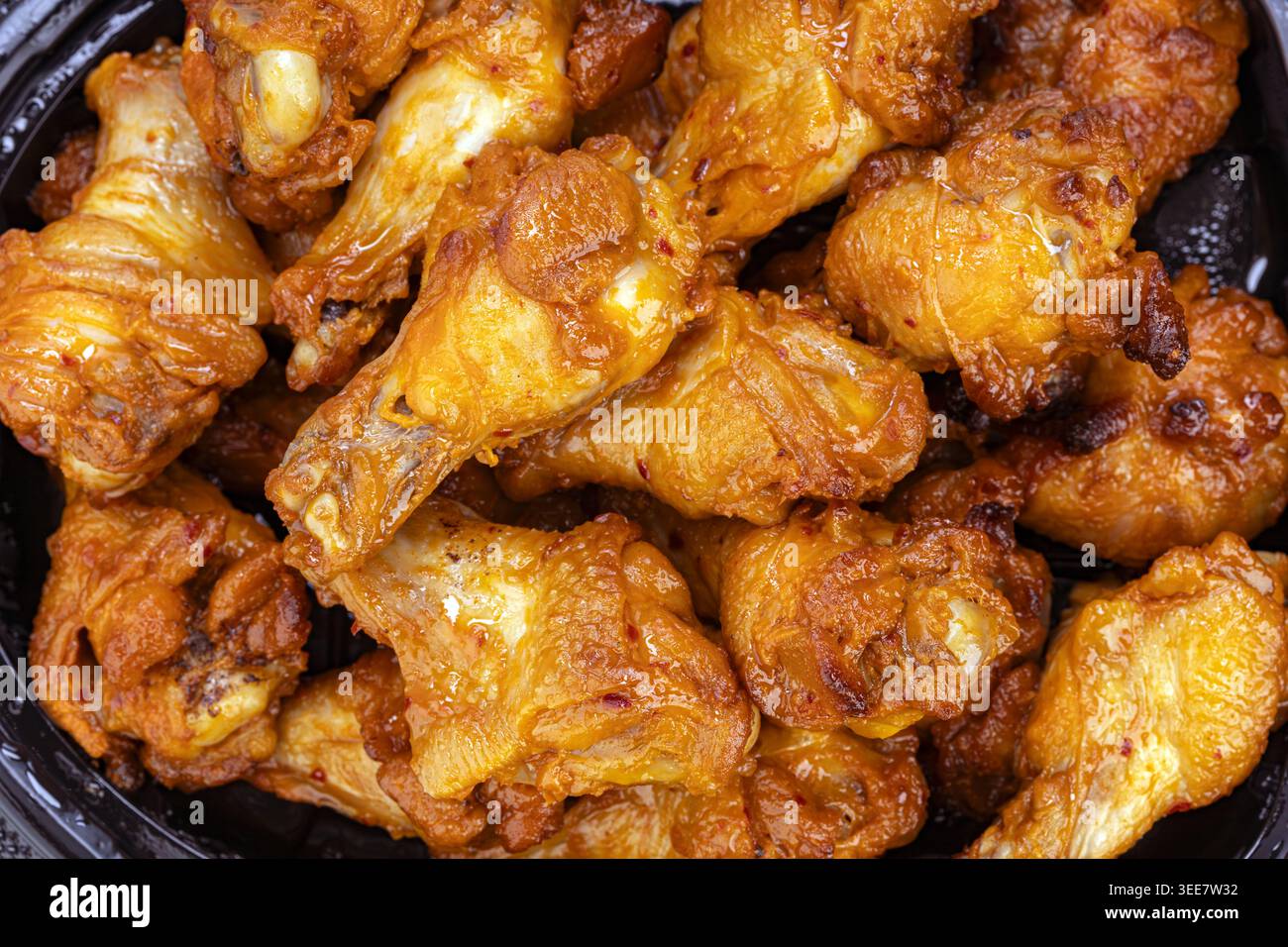 Vista ravvicinata di tamburi di pollo grigliati caldi e piccanti impilati in una ciotola buia. Ogni pezzo è ricoperto da una salsa ricca e lucida con un'arancia dorata Foto Stock