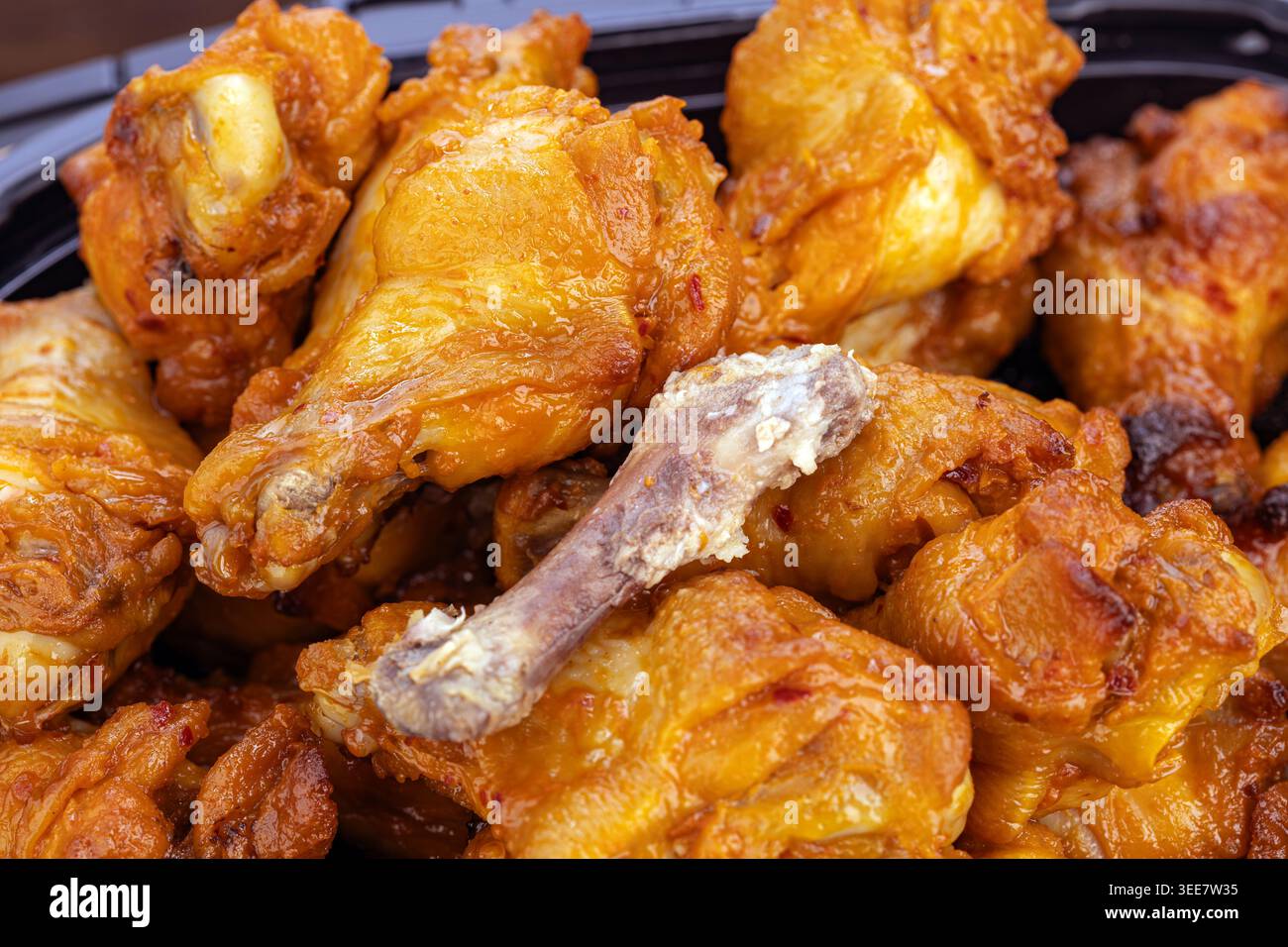 Vista ravvicinata delle drumette di pollo alla griglia calde e piccanti accumulate generosamente in un vassoio nero La carne tenera e succosa è ricoperta da un'audace e lucida sa piccante Foto Stock
