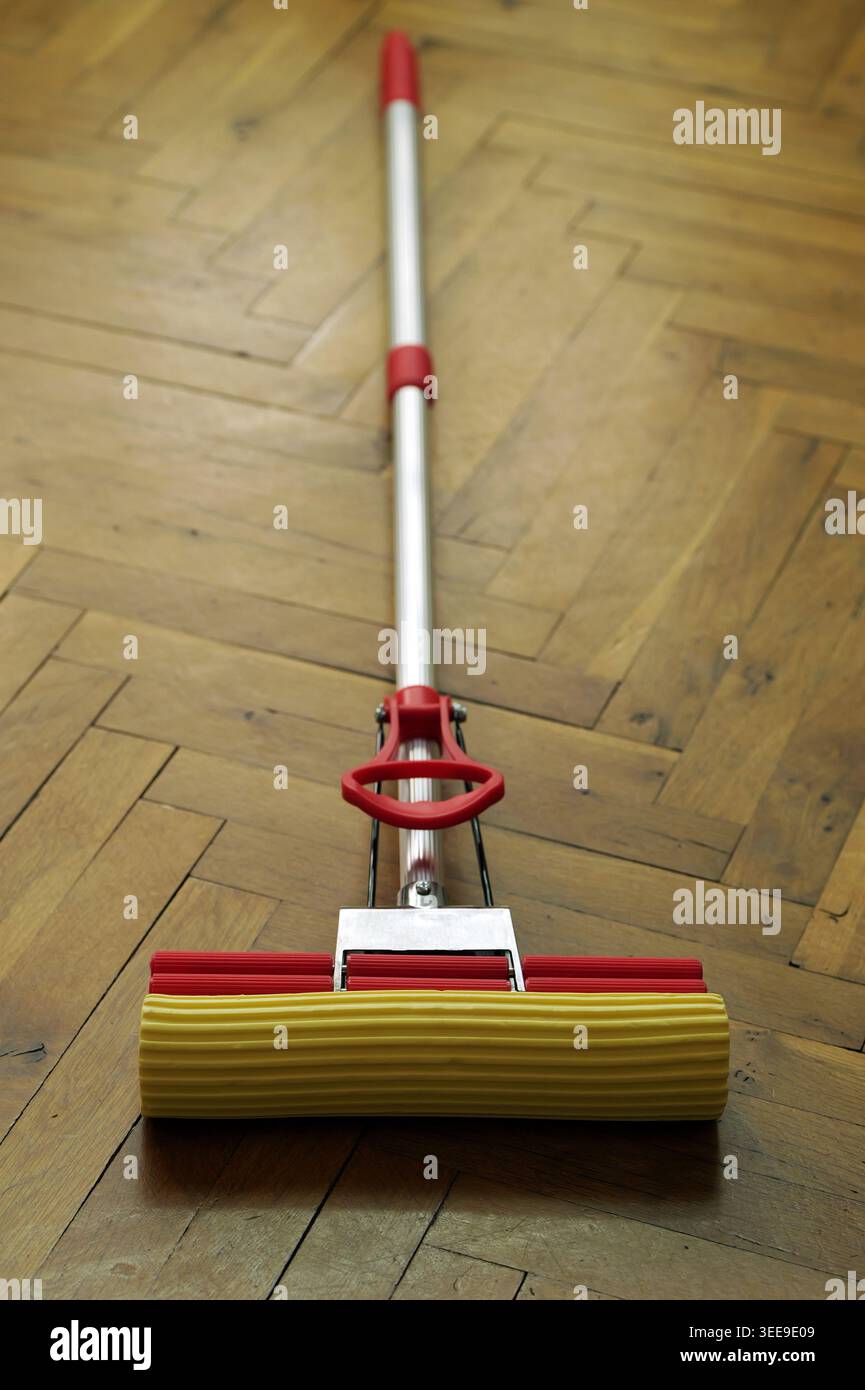Scopa in spugna rossa e gialla appoggiata su un pavimento in legno marrone chiaro, pronta per la pulizia e le faccende domestiche Foto Stock