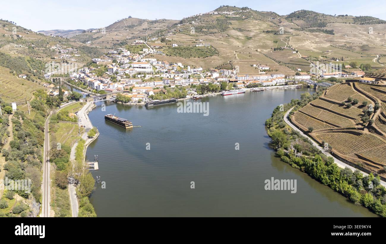 Vista aerea della città di Pinhao, annidata lungo il fiume Douro, con vigneti terrazzati su colline ondulate e barche da crociera attraccate sul lungomare Foto Stock
