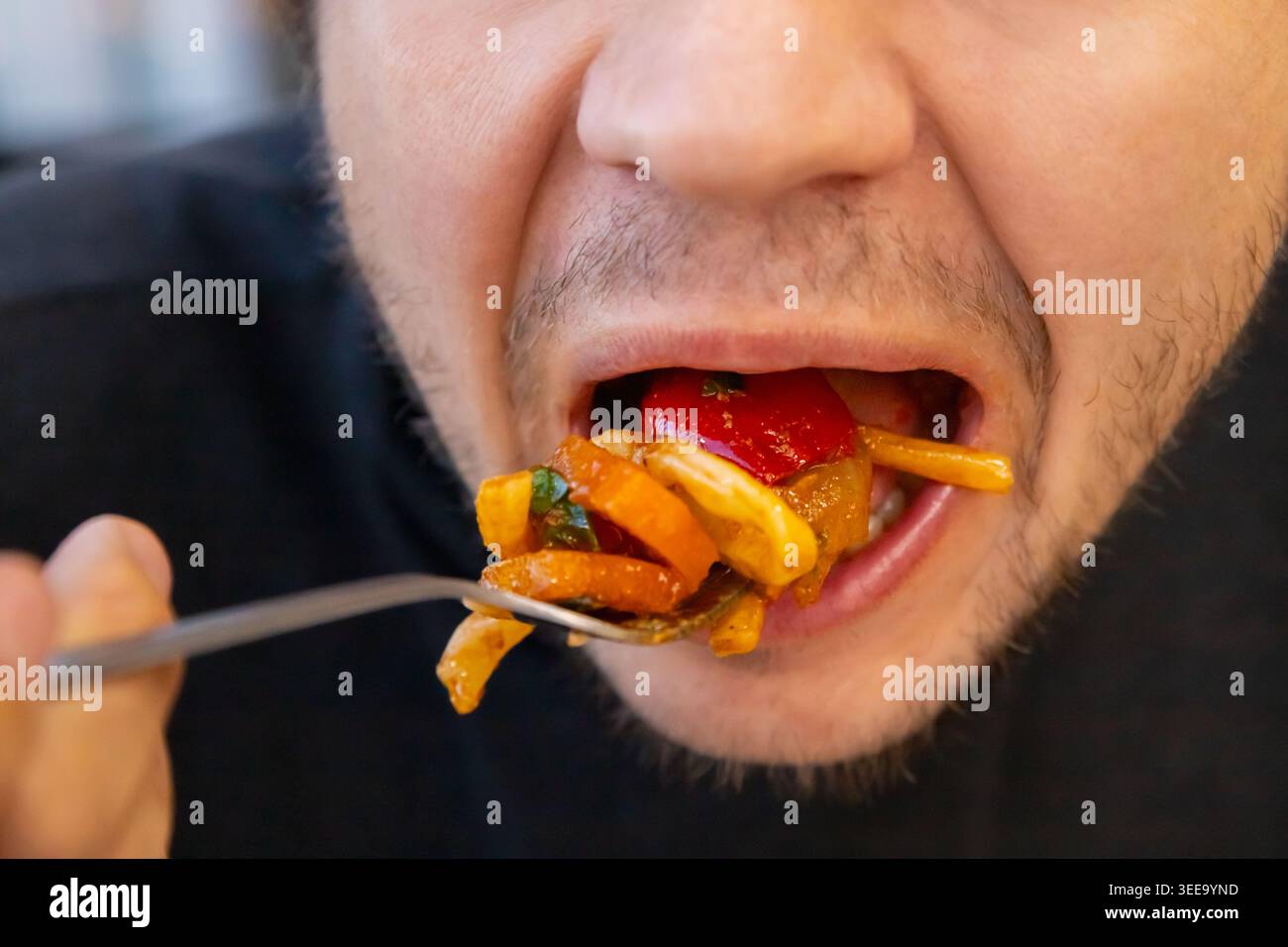 maschio che mangia una grande forkful di verdure fritte in padella con la bocca aperta, mostrando abitudini alimentari troppo alimentari e malsane. concetto di obesità, diabete Foto Stock