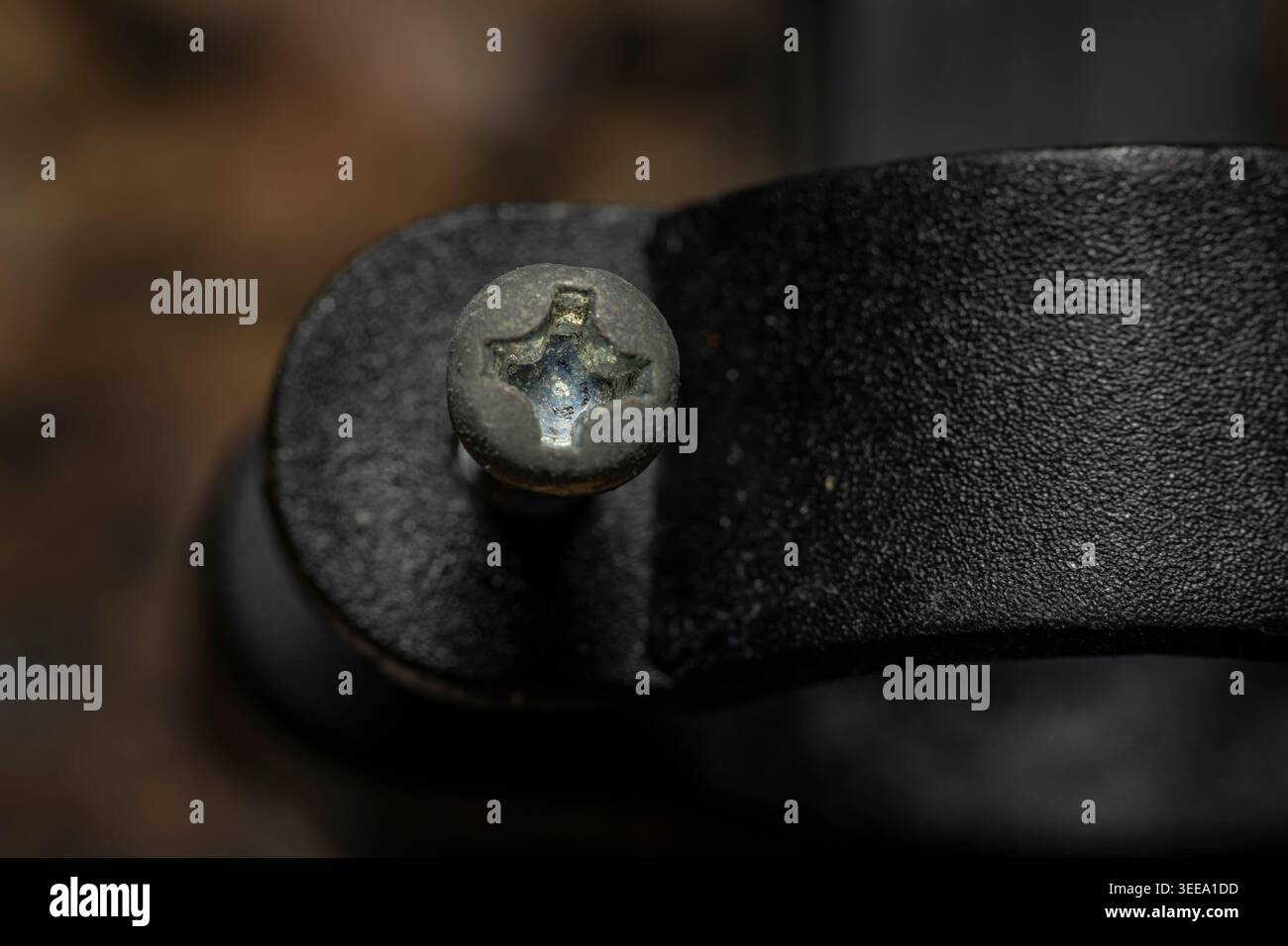 Vista dall'alto macro estrema di una singola vite in metallo con testa a croce fissata in una staffa di montaggio nera con sfondo bokeh morbido Foto Stock
