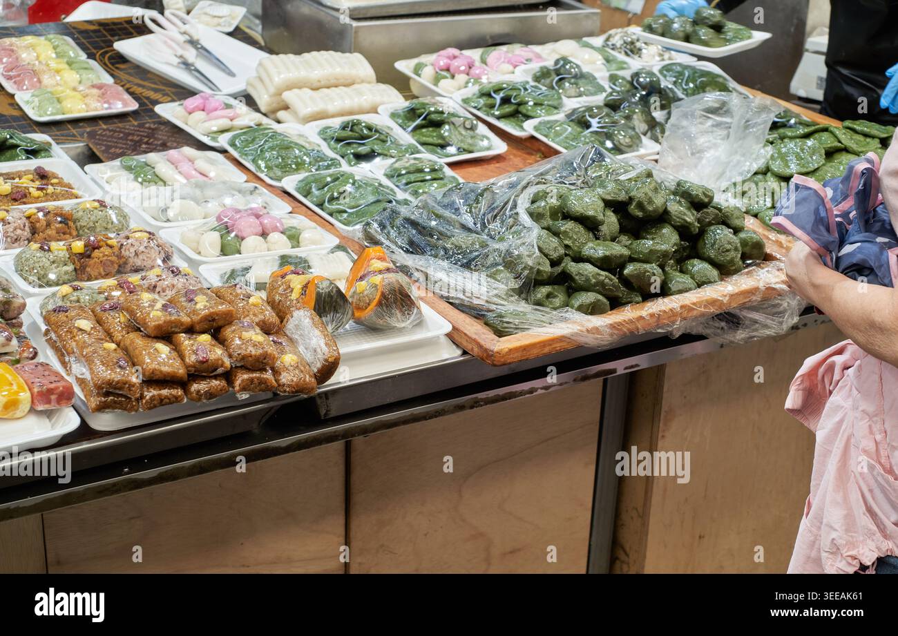 Un vivace mercato coreano ripieno di tradizionali torte di riso. I colorati songpyeon e yaksik catturano l'autentica essenza della cultura gastronomica locale. Foto Stock