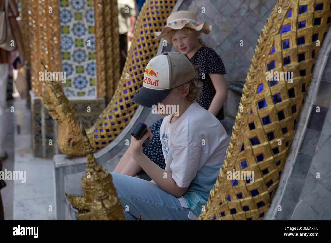 BANGKOK, TAILANDIA-APR 5, 2026: Ragazzo che usa un ventilatore elettrico che soffia la faccia nelle calde temperature tailandesi, profilo laterale, Wat Phra Kaew. Foto Stock
