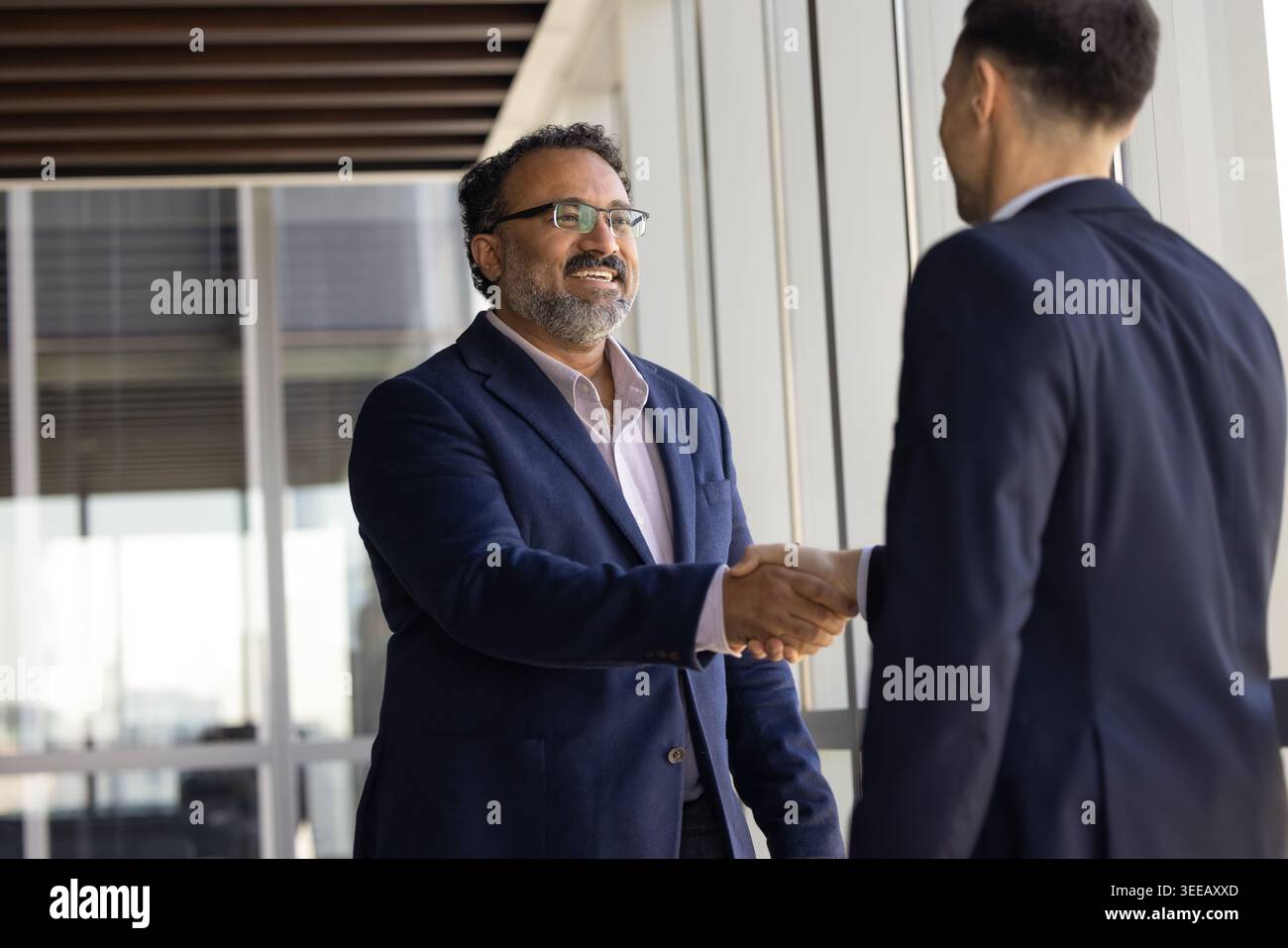 Due uomini d'affari sorridenti che stringono la mano nell'ufficio della compagnia Foto Stock