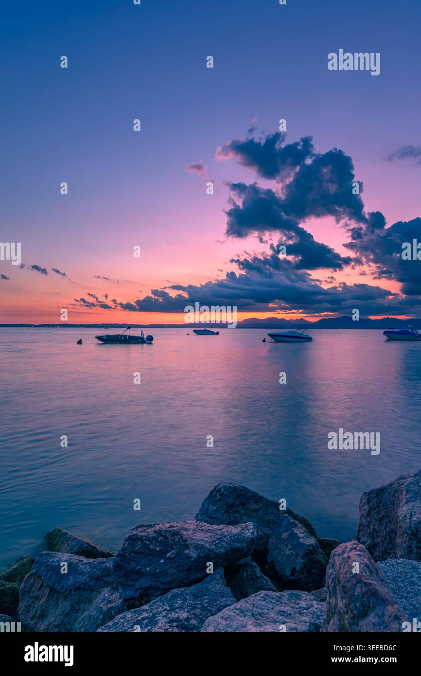 Tramonto sereno sul Lago di Garda con barche e Rocky Shore Foto Stock