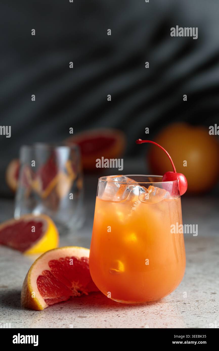 Cocktail con ghiaccio e succo di pompelmo. Bere con ghiaccio nel bicchiere congelato e frutta fresca su un tavolo di pietra. Sullo sfondo, le ombre del palmo leav Foto Stock