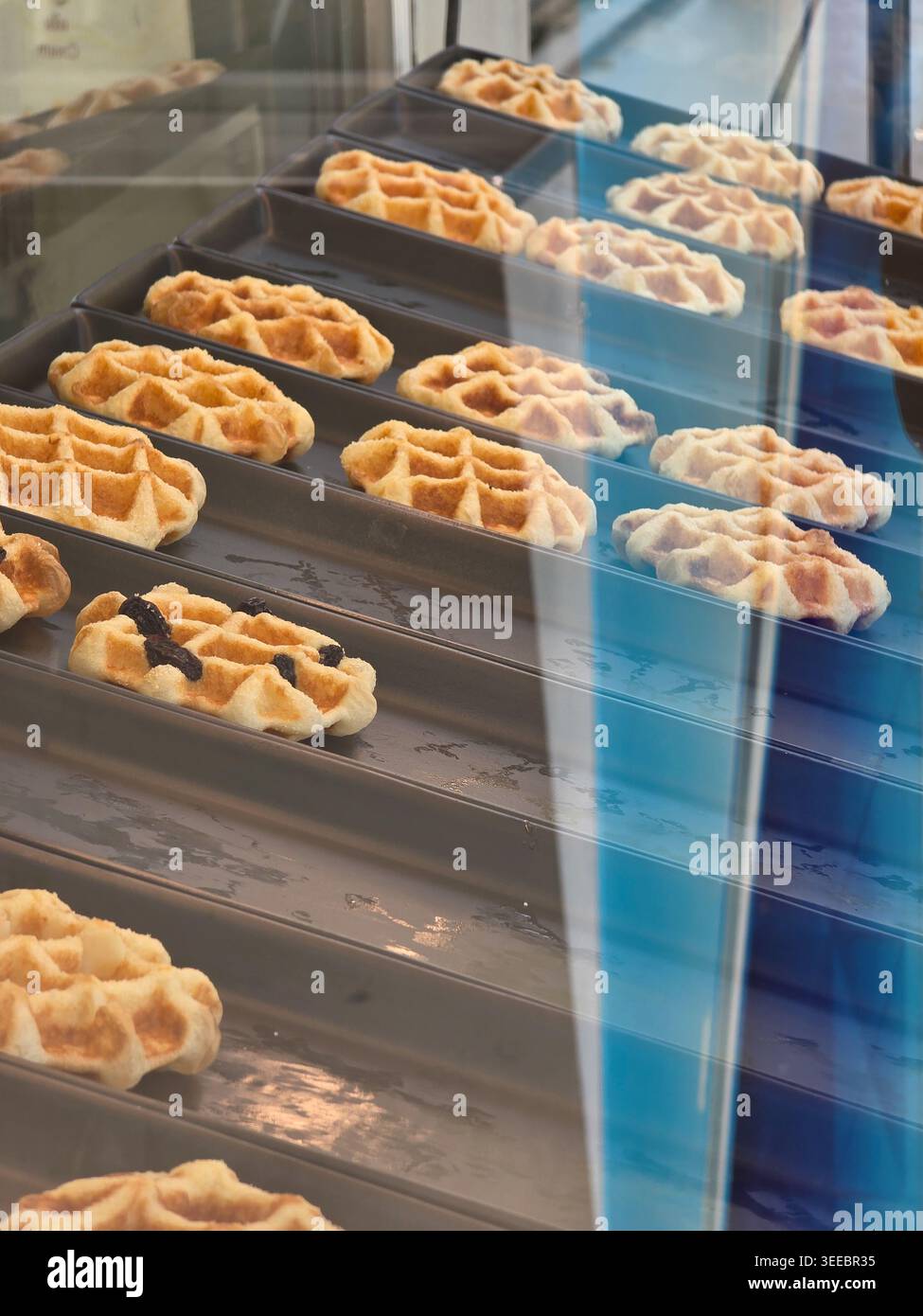 La pasticceria a base di waffle freschi all'interno della vetrina della panetteria offre deliziosi e deliziosi spuntini al forno. I dolcetti dorati si trovano sul vassoio dietro la finestra di vetro Foto Stock