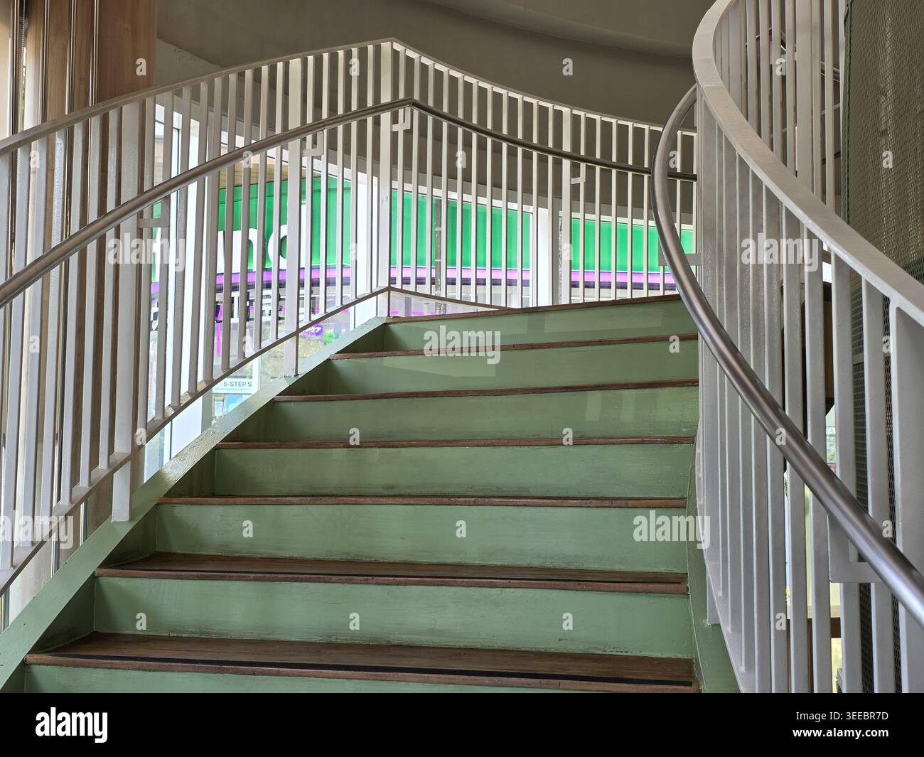 Moderna scalinata curva interna con ringhiera in metallo bianco e gradini verdi che salgono verso l'alto a creare un ambiente interno tranquillo e strutturato Foto Stock