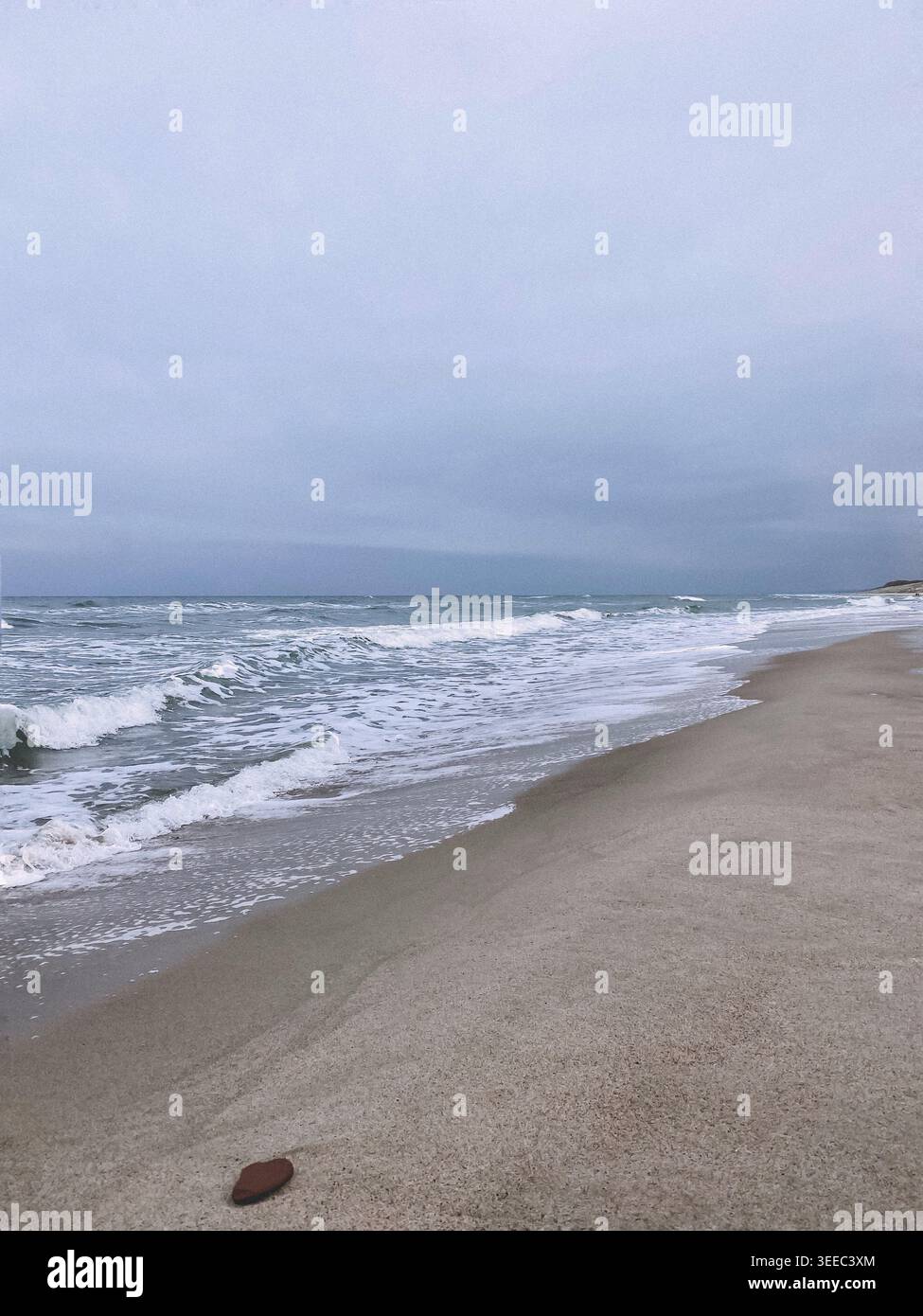 Spiaggia di sabbia vuota con onde morbide sotto il cielo nuvoloso, paesaggio costiero minimale con atmosfera tranquilla e suggestiva - Immagine stock catturata con smartphone
