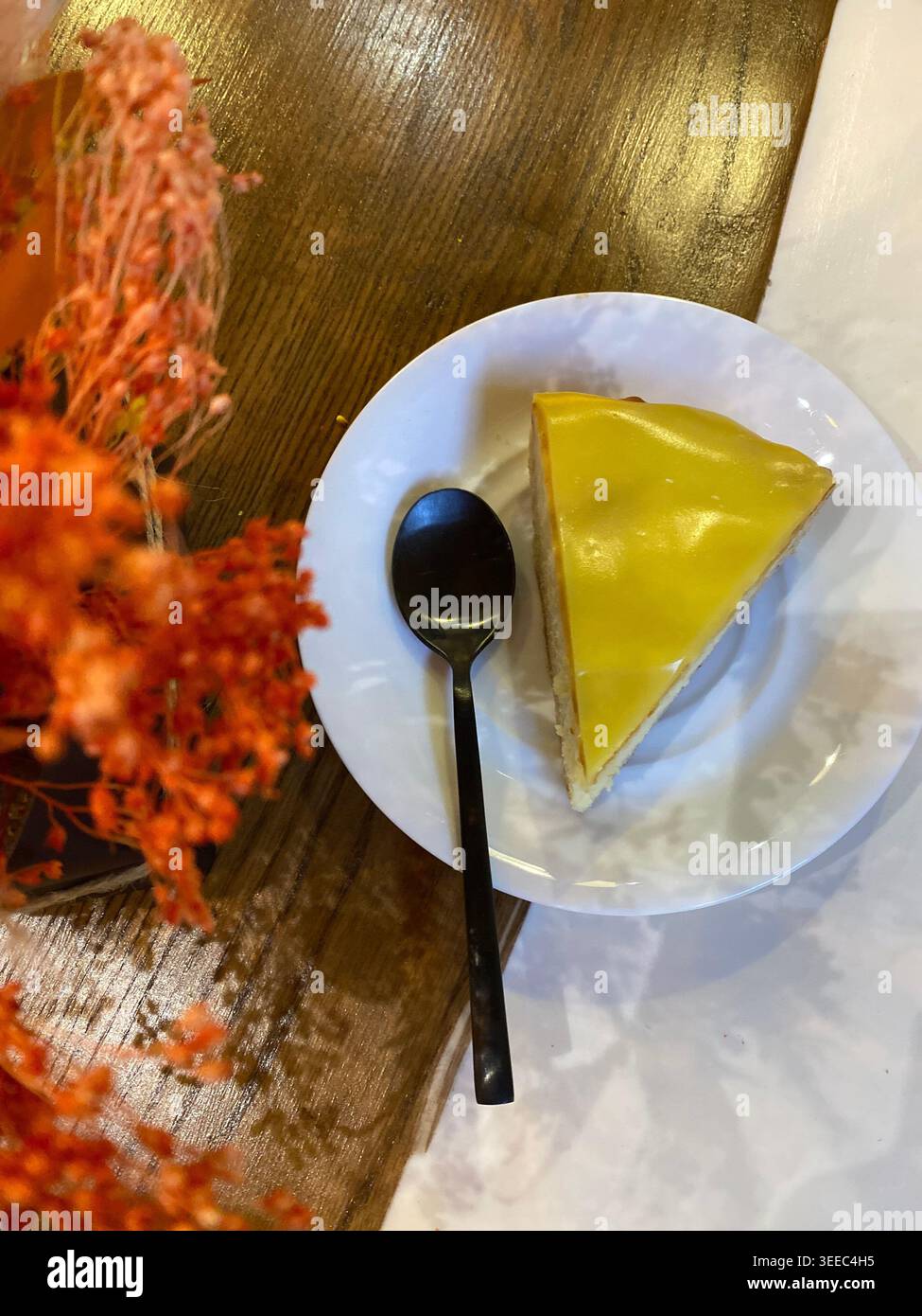Fetta di cheesecake al limone su un piatto bianco con cucchiaio, accogliente tavolino da caffè - Immagine stock catturata con smartphone