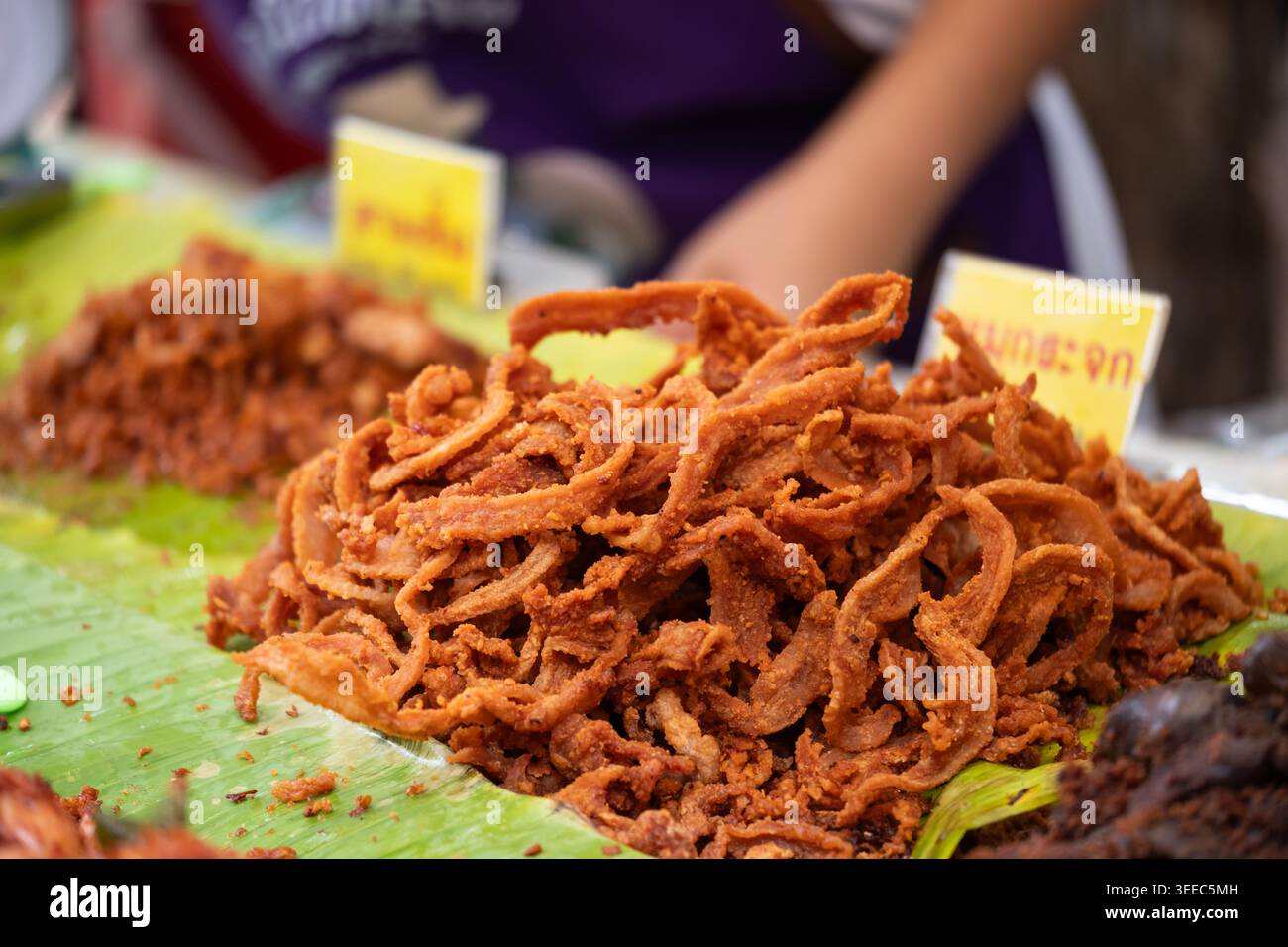 Fritte in profondità, croccanti strisce di pancia di maiale, un popolare spuntino thailandese chiamato "Moo Krachok", impilato su foglie di banana in un mercato di strada. Foto Stock