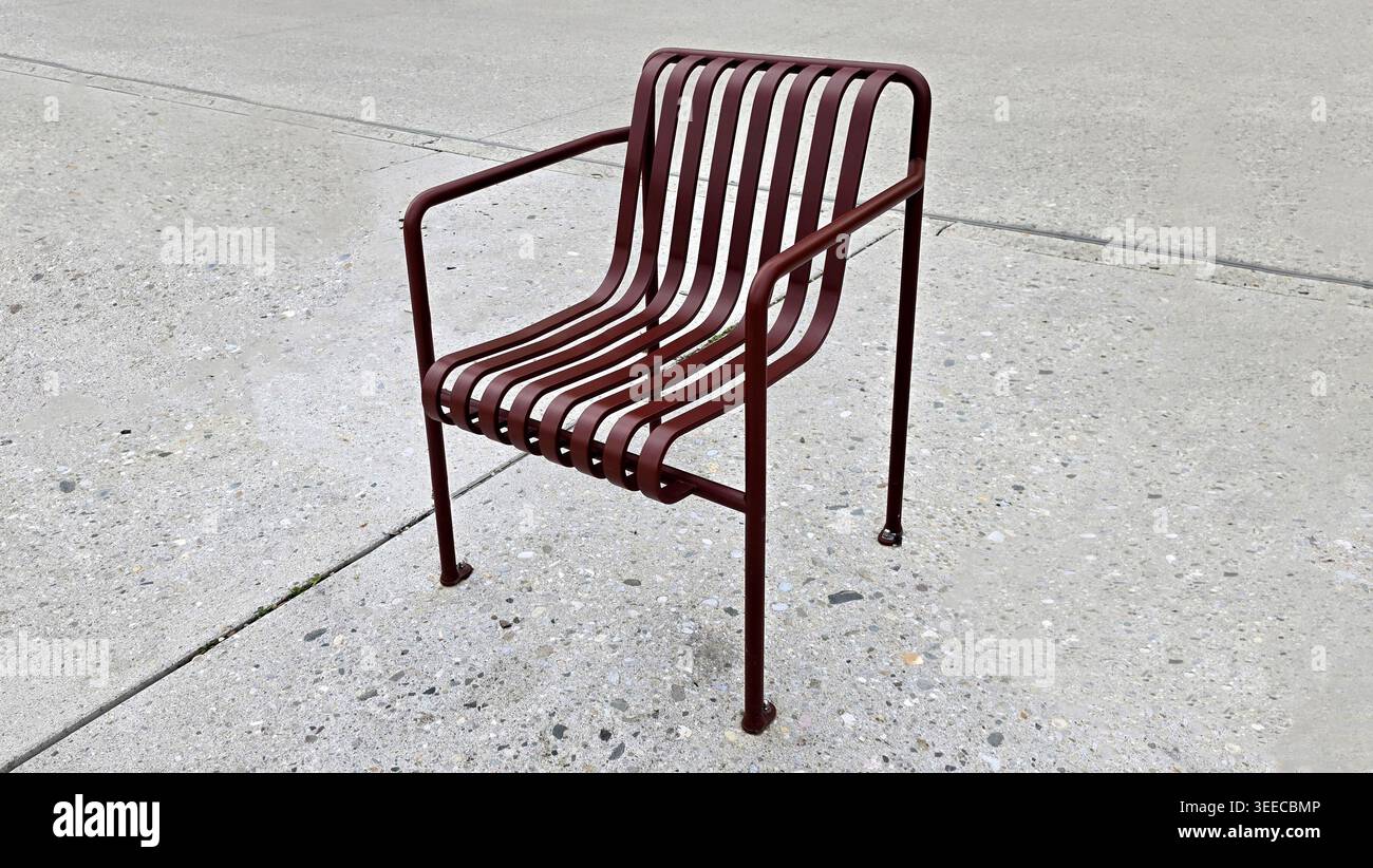 Una sedia da esterno minimalista e contemporanea, realizzata con spranghe in metallo marrone curvo e una sottile struttura tubolare, si erge da sola su un cemento grigio chiaro macchiato Foto Stock