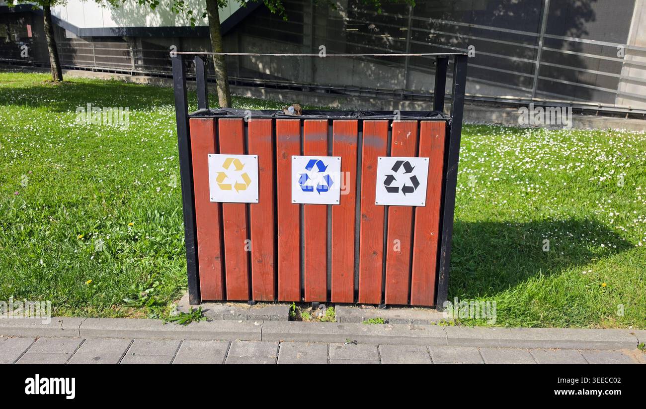 Una stazione funzionale di smistamento dei rifiuti realizzata con piastre in legno rossastro presenta simboli di riciclaggio gialli, blu e neri per lo smaltimento segregato in pubblico Foto Stock