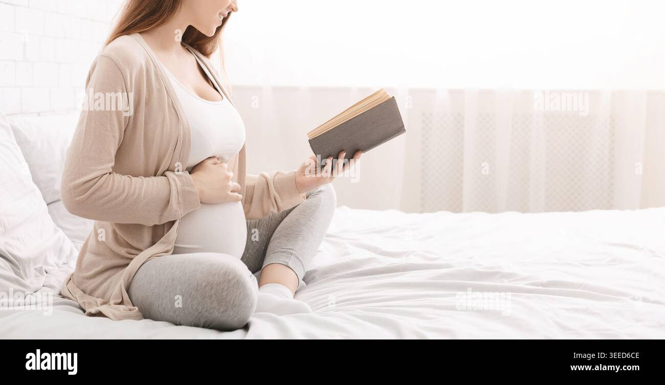 Bella donna incinta leggendo un libro sul letto Foto Stock