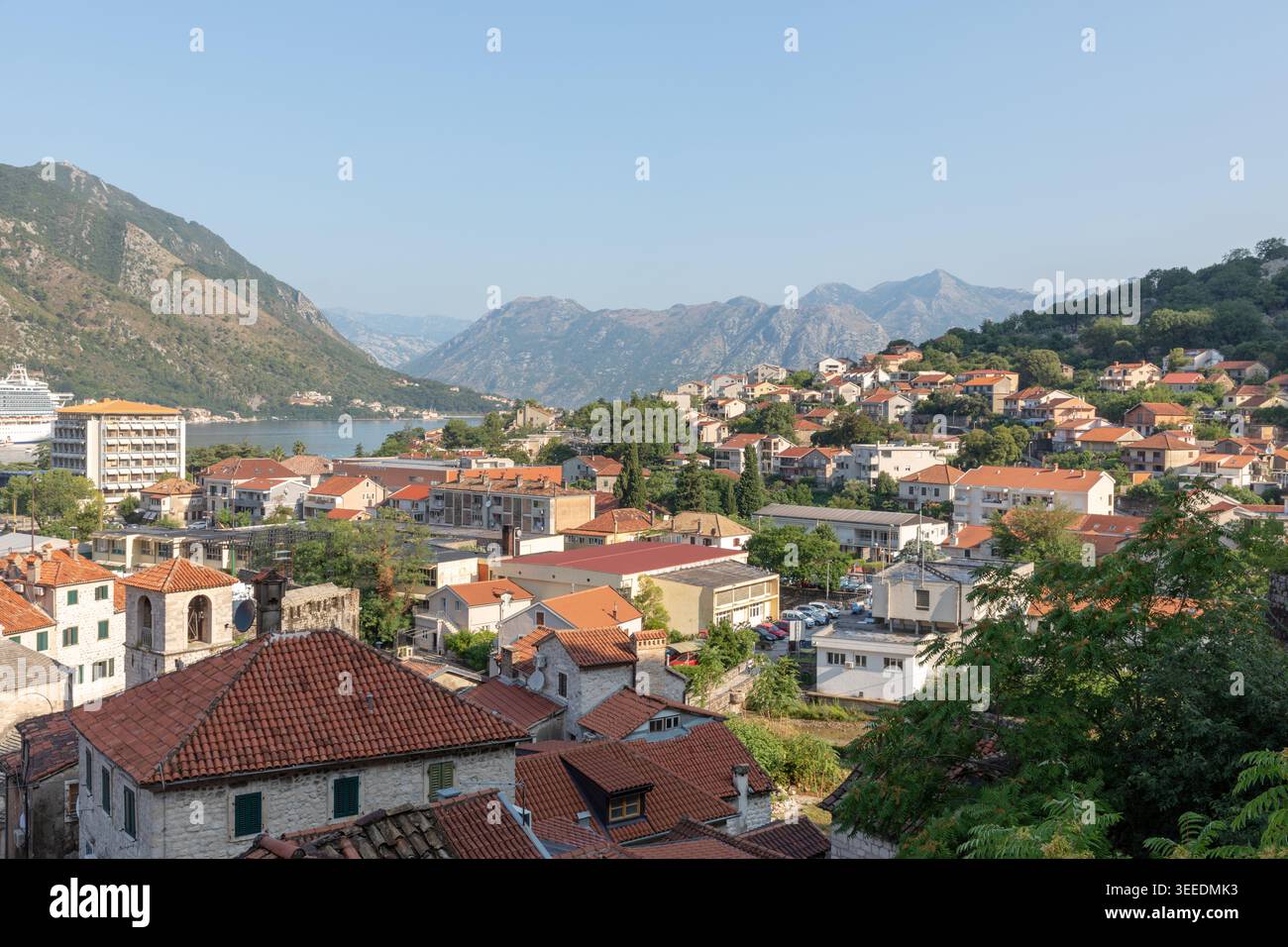 Vista panoramica sopraelevata sui tetti di tegole rosse e sugli edifici in pietra a Cattaro, con la baia di Cattaro e le aspre montagne sullo sfondo, Montenegro Foto Stock